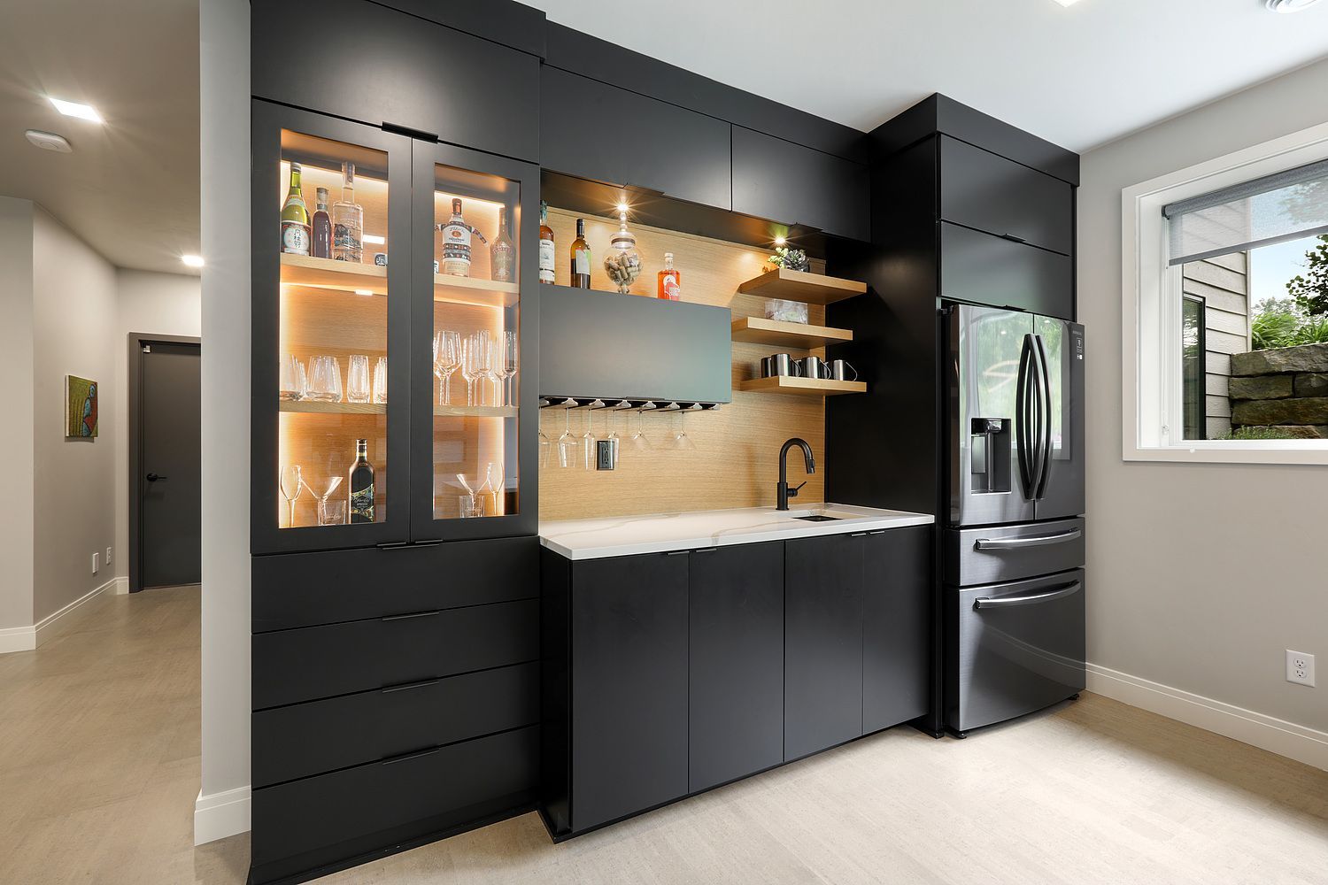 Modern black home bar with built-in cabinetry, refrigerator, sink, and shelves; lighted display cabinet.