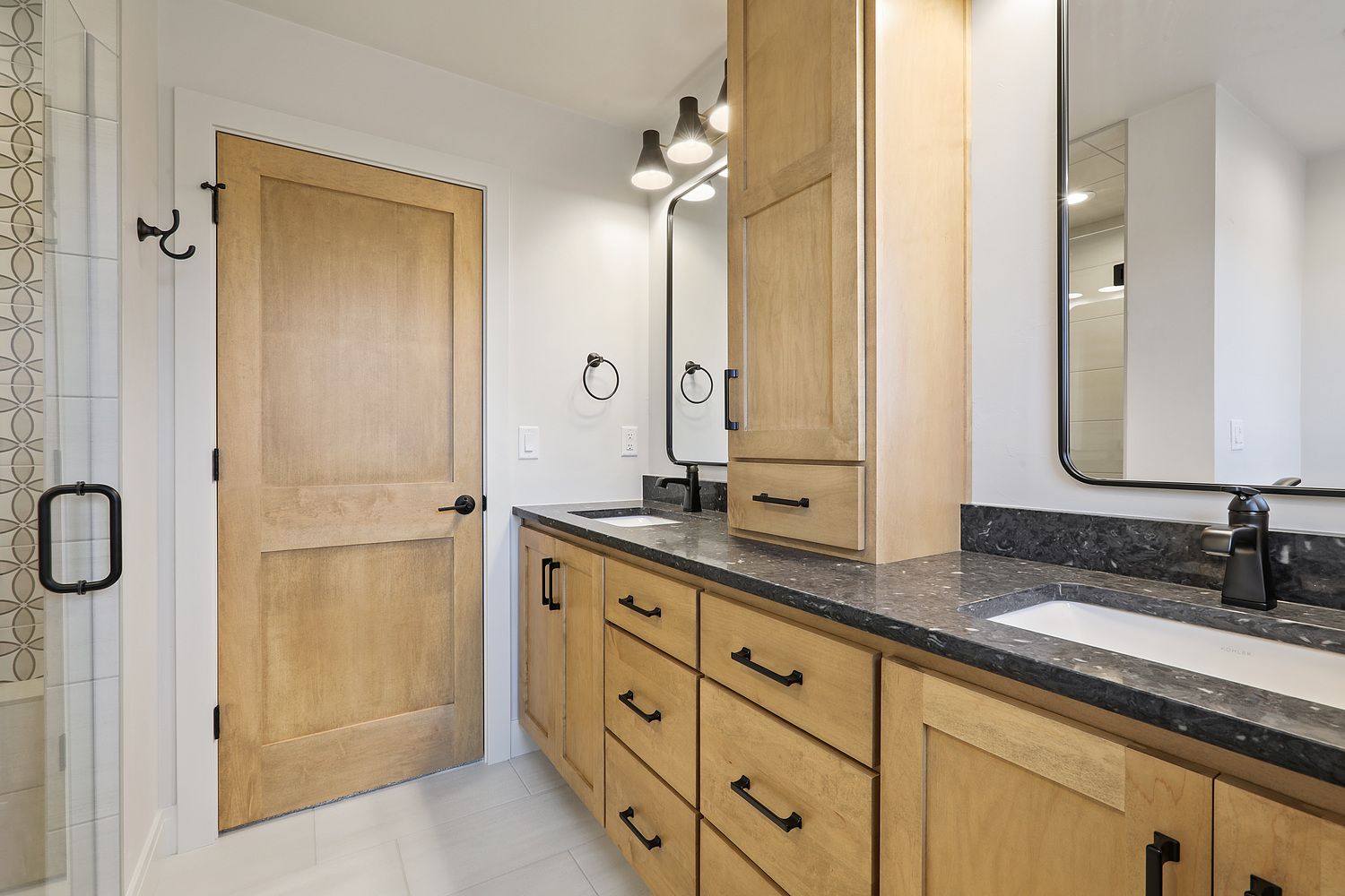 Bathroom with wooden cabinets, black accents, white counters, and a tall cabinet.