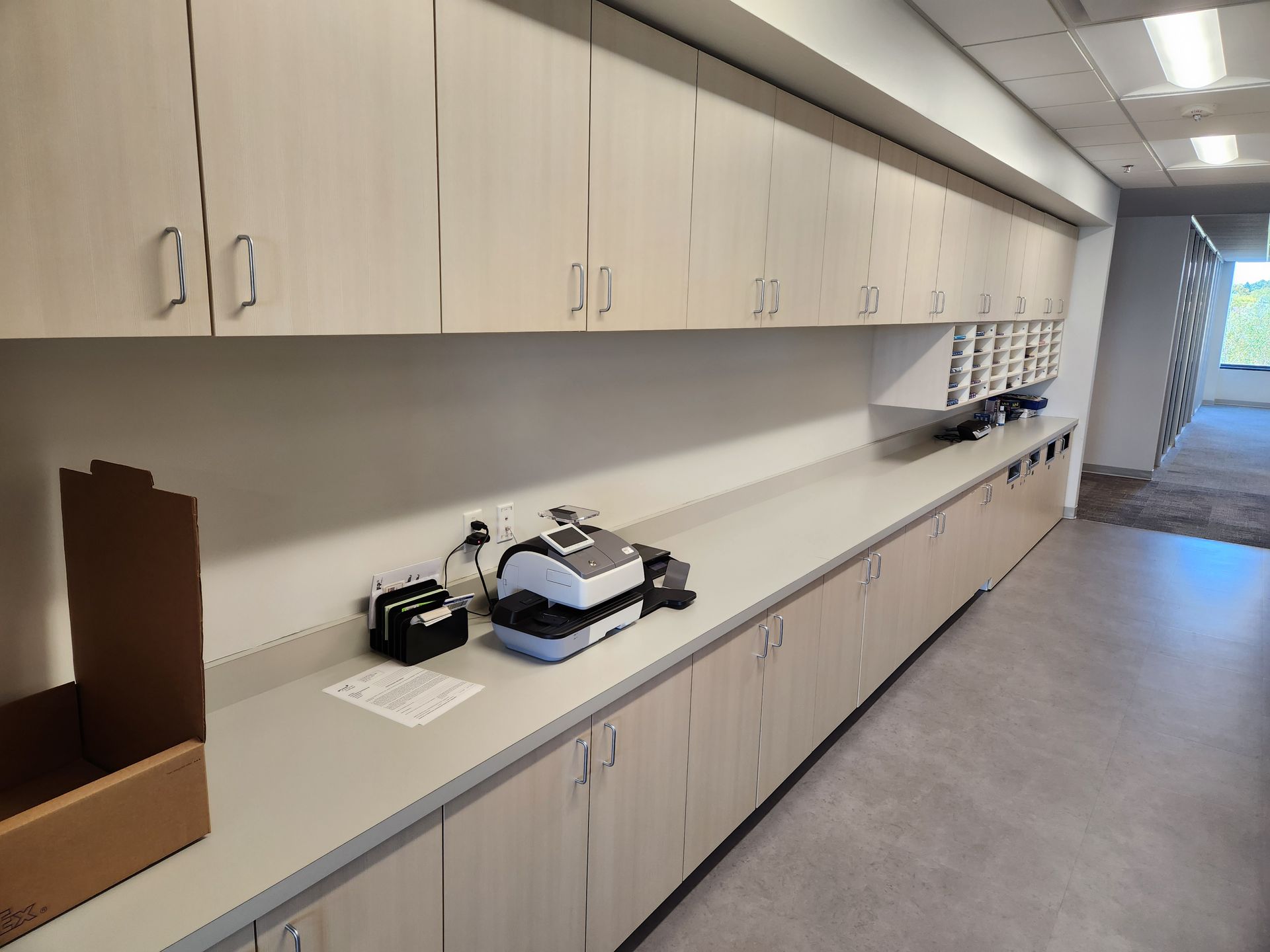 Long, light-colored cabinets line a hallway wall. A long countertop holds equipment.
