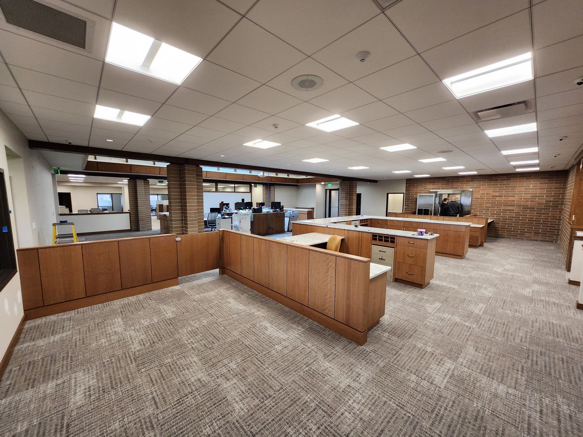 Open office space with rows of desks, carpeted floor, and exposed brick wall.