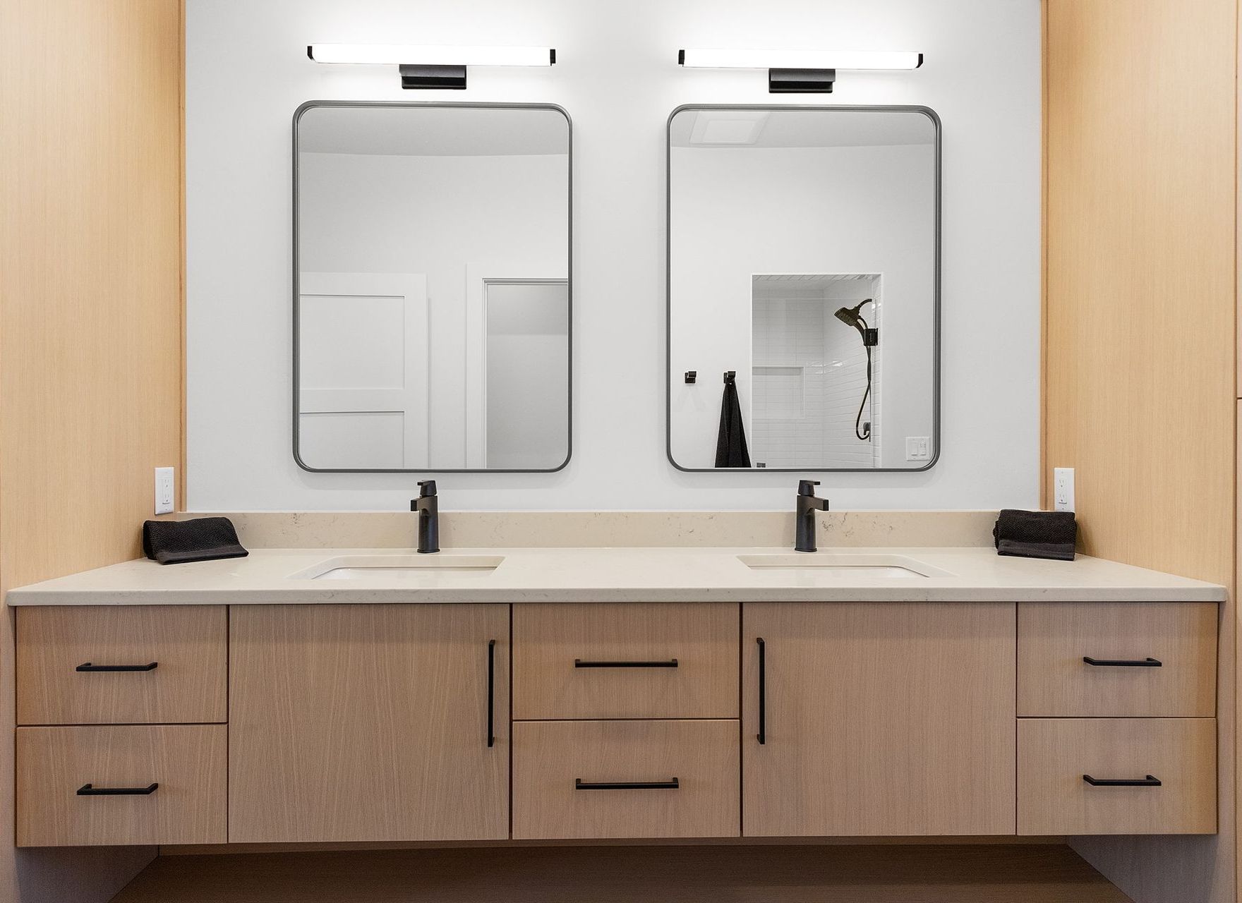 Bathroom with two mirrors over a light-colored vanity, black faucets, and neutral walls.
