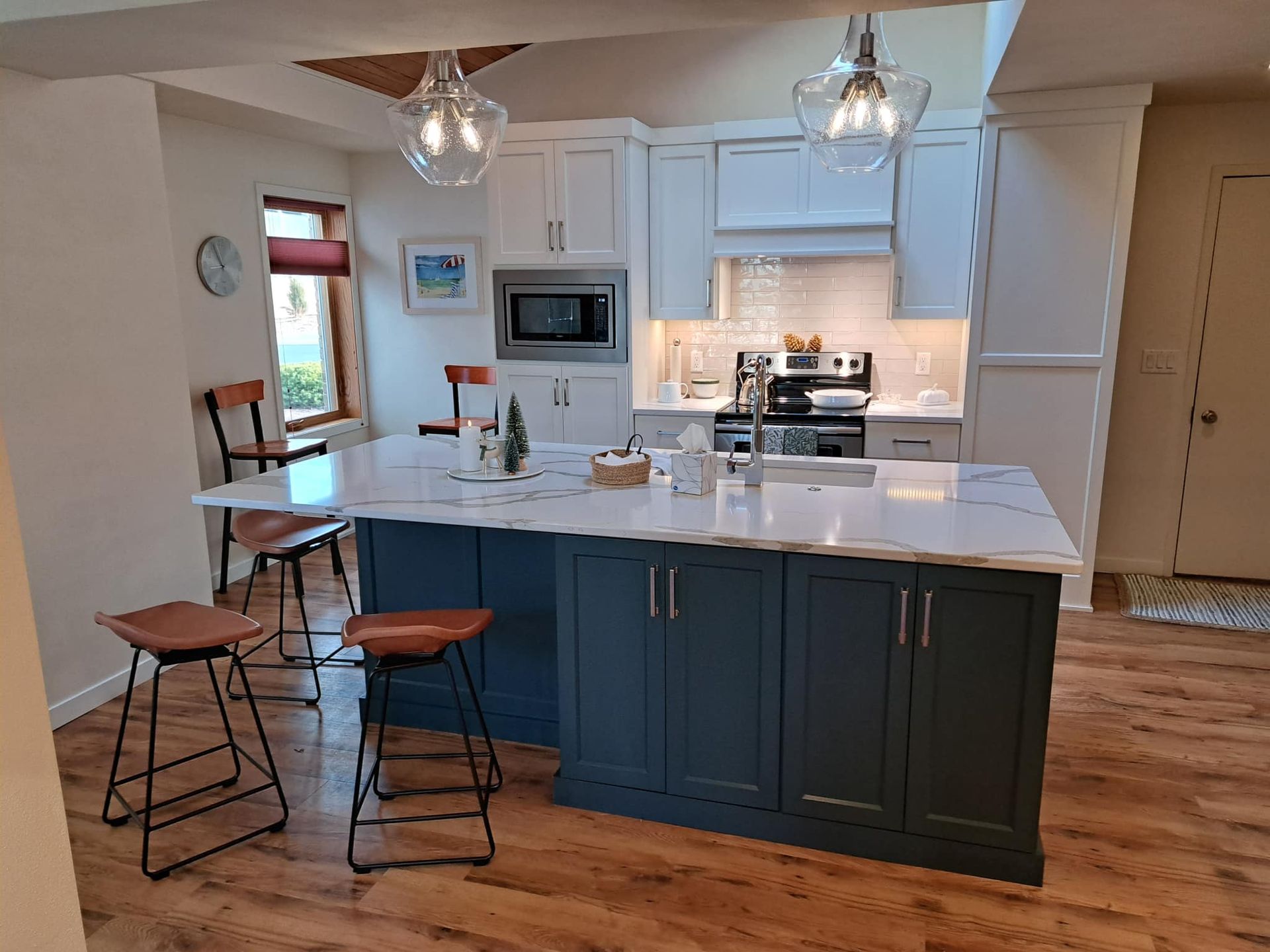 Kitchen with blue island and white countertops; wood floors, white cabinets, and two pendant lights.