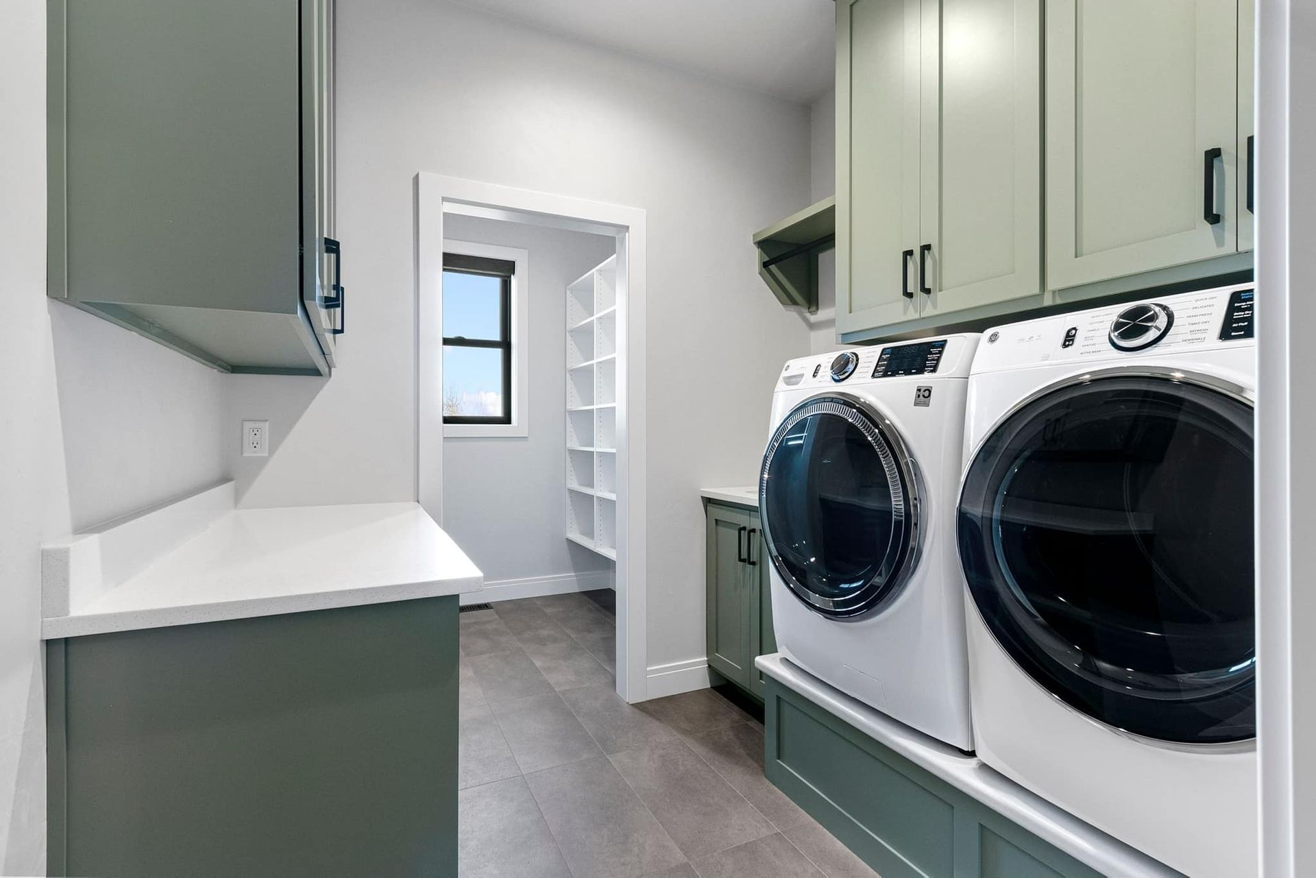Laundry room with sage green cabinets, white appliances, and pantry.