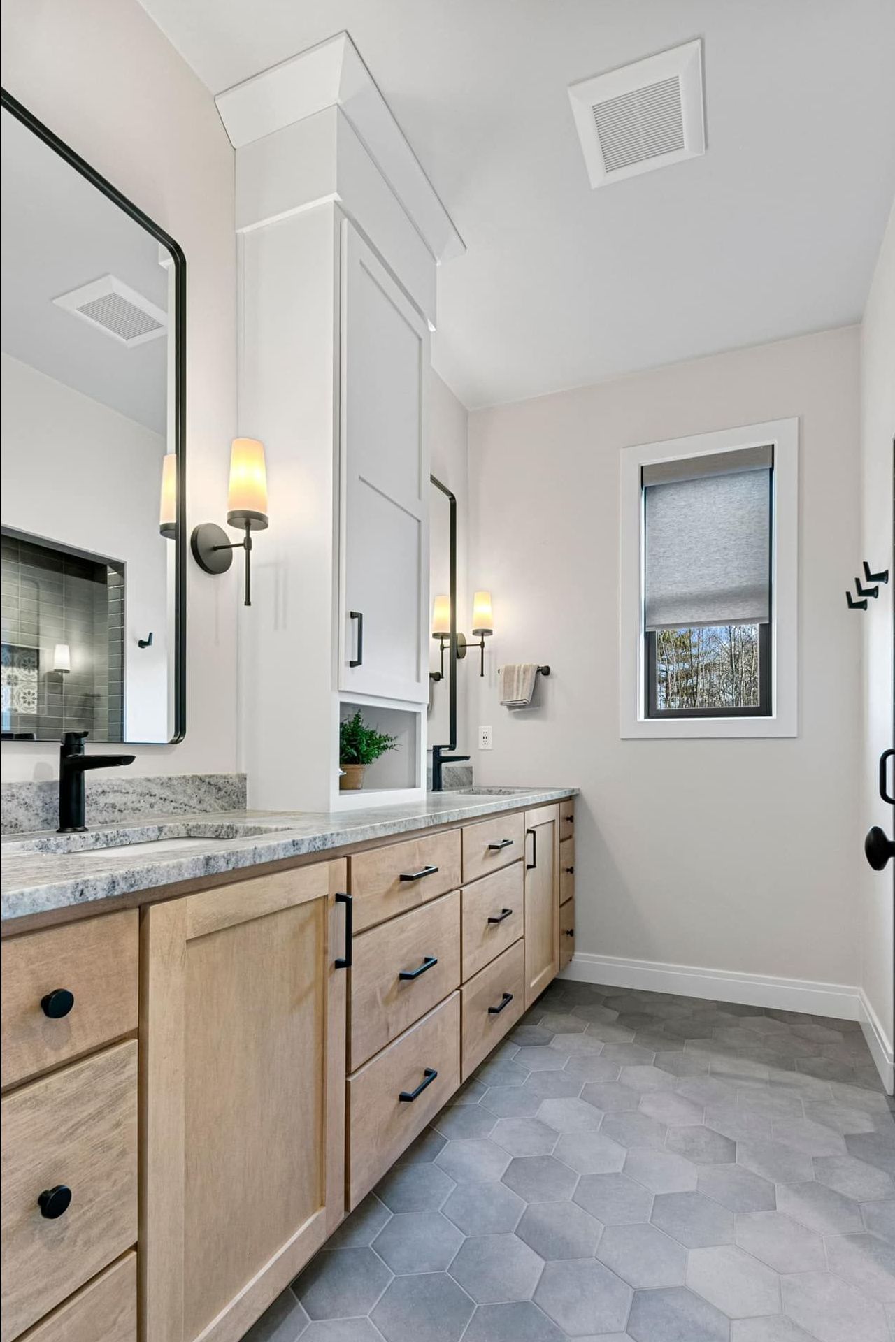 A bathroom with two sinks , a mirror , and a window.