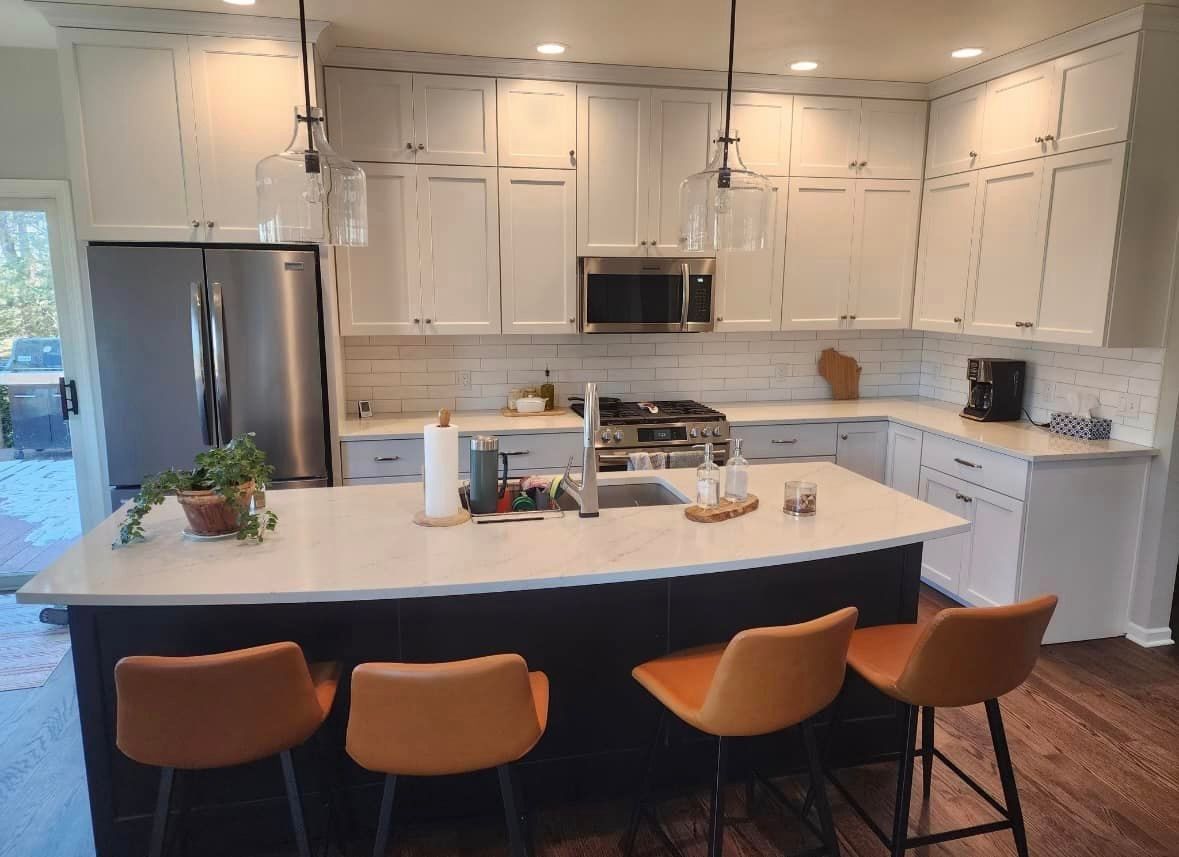 Modern kitchen with white cabinets, dark blue island, and orange bar stools.