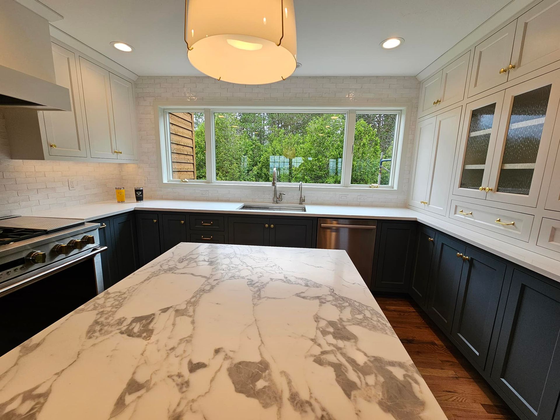 Kitchen with marble island, dark blue cabinets, white countertops, and a large window.