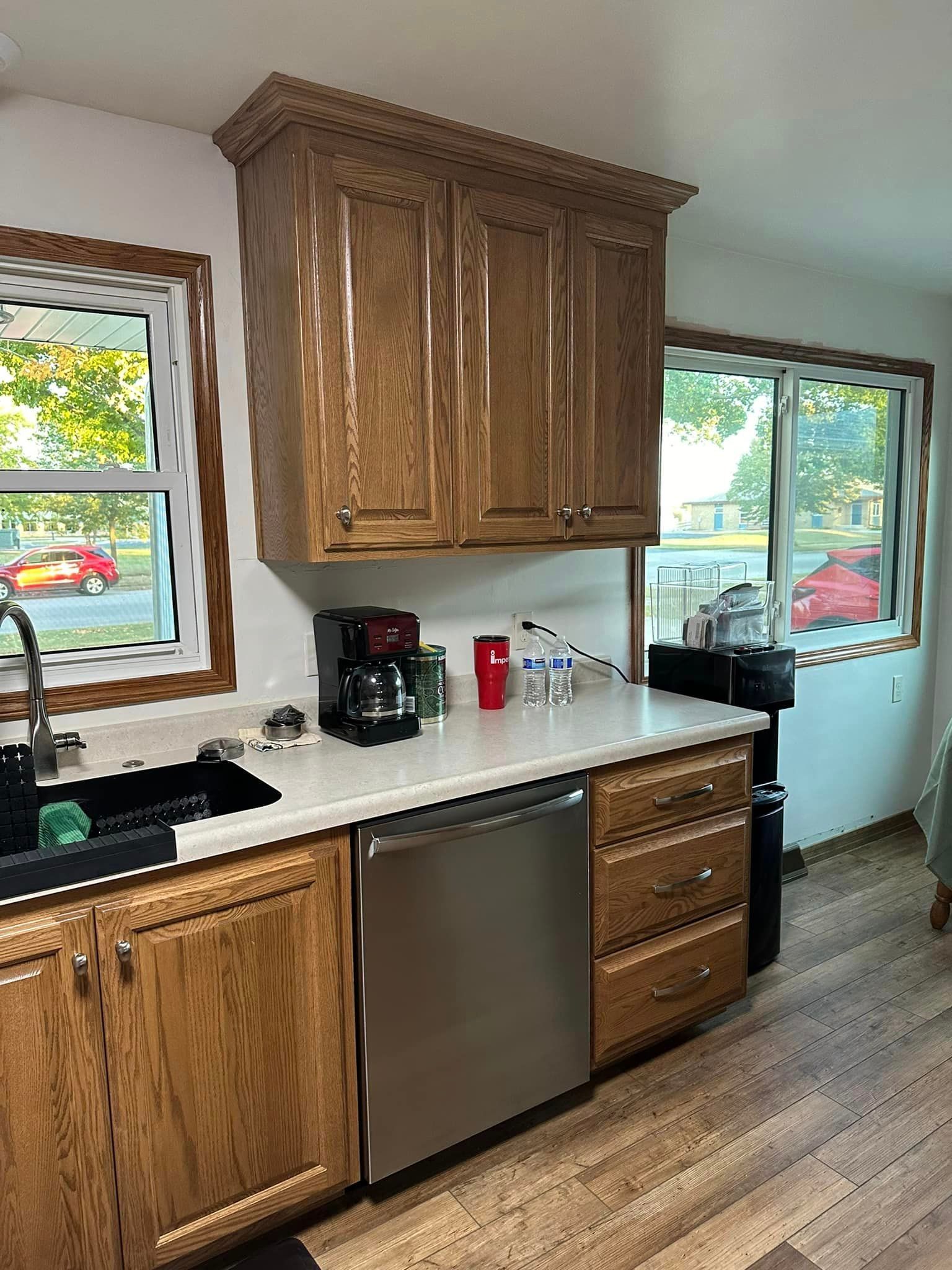 Kitchen with brown cabinets, stainless steel dishwasher, white countertops, and windows.