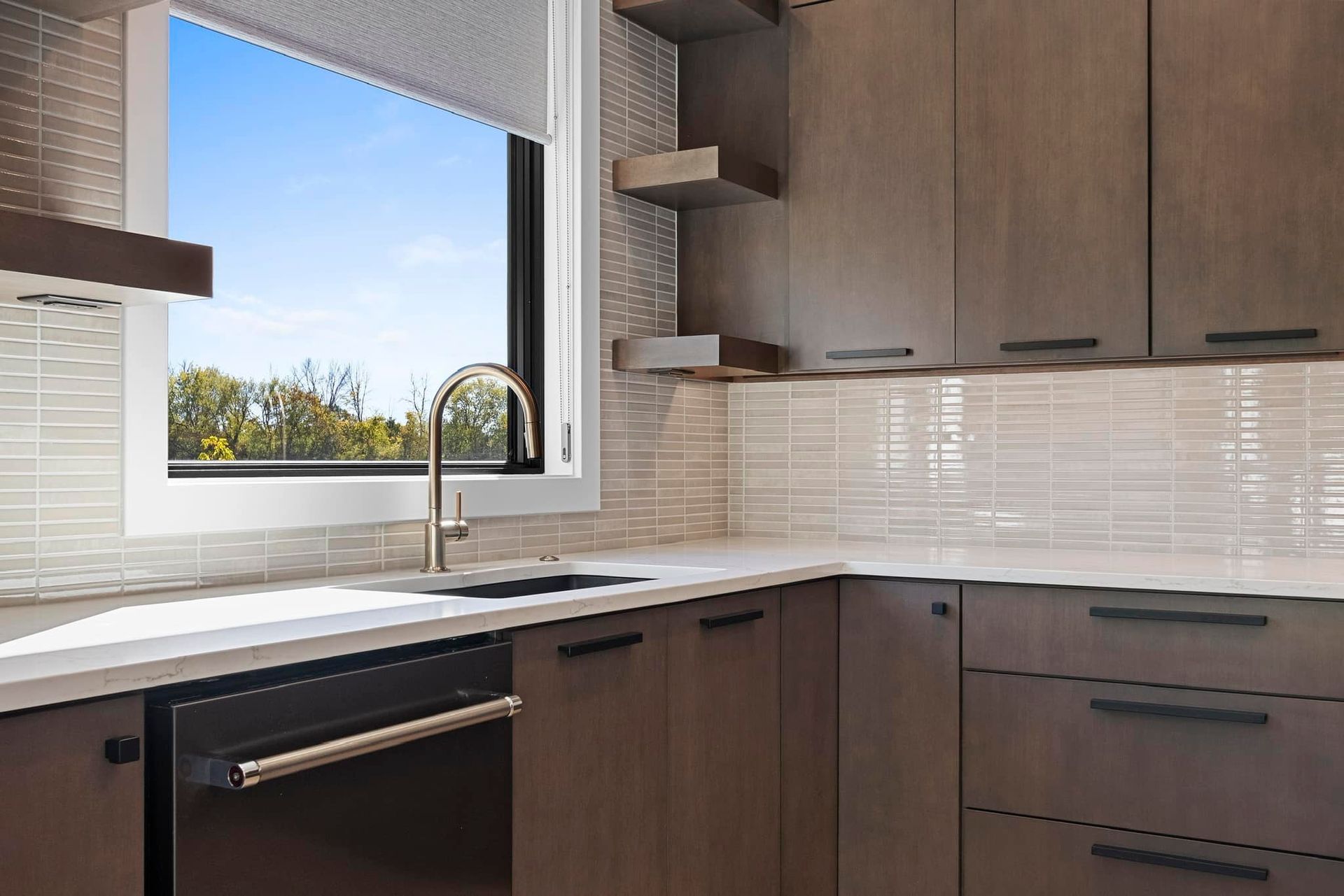 Modern kitchen with grey cabinets, stainless steel appliances, and a view of trees through a window.