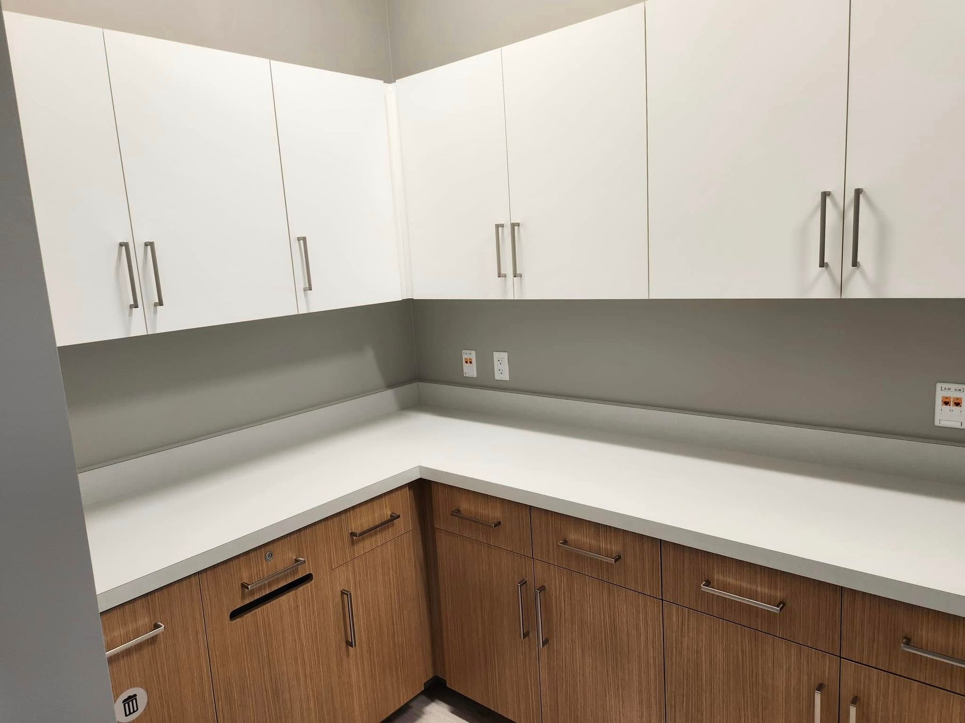 White and wood-tone cabinets in a corner, with a white countertop and gray walls.