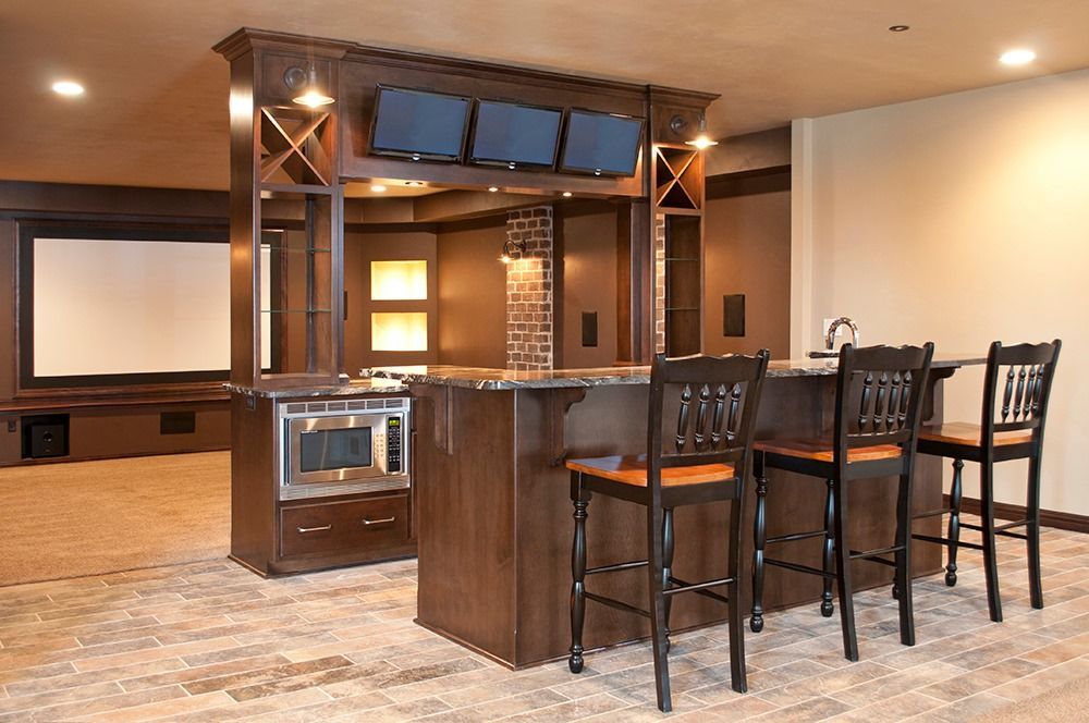 A basement with a bar , chairs and a projector screen.