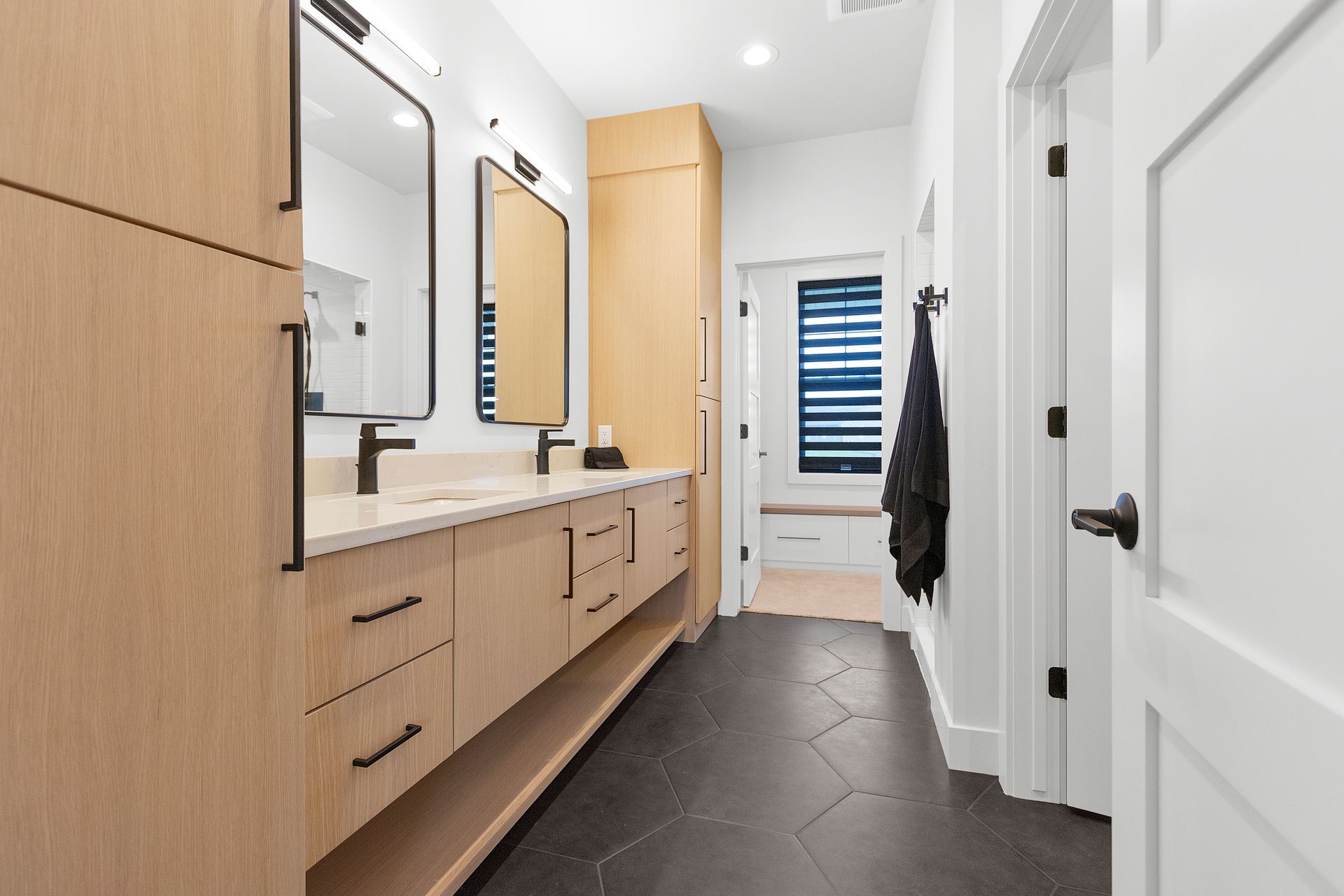 Modern bathroom with wood vanity, black fixtures, and patterned dark floor.