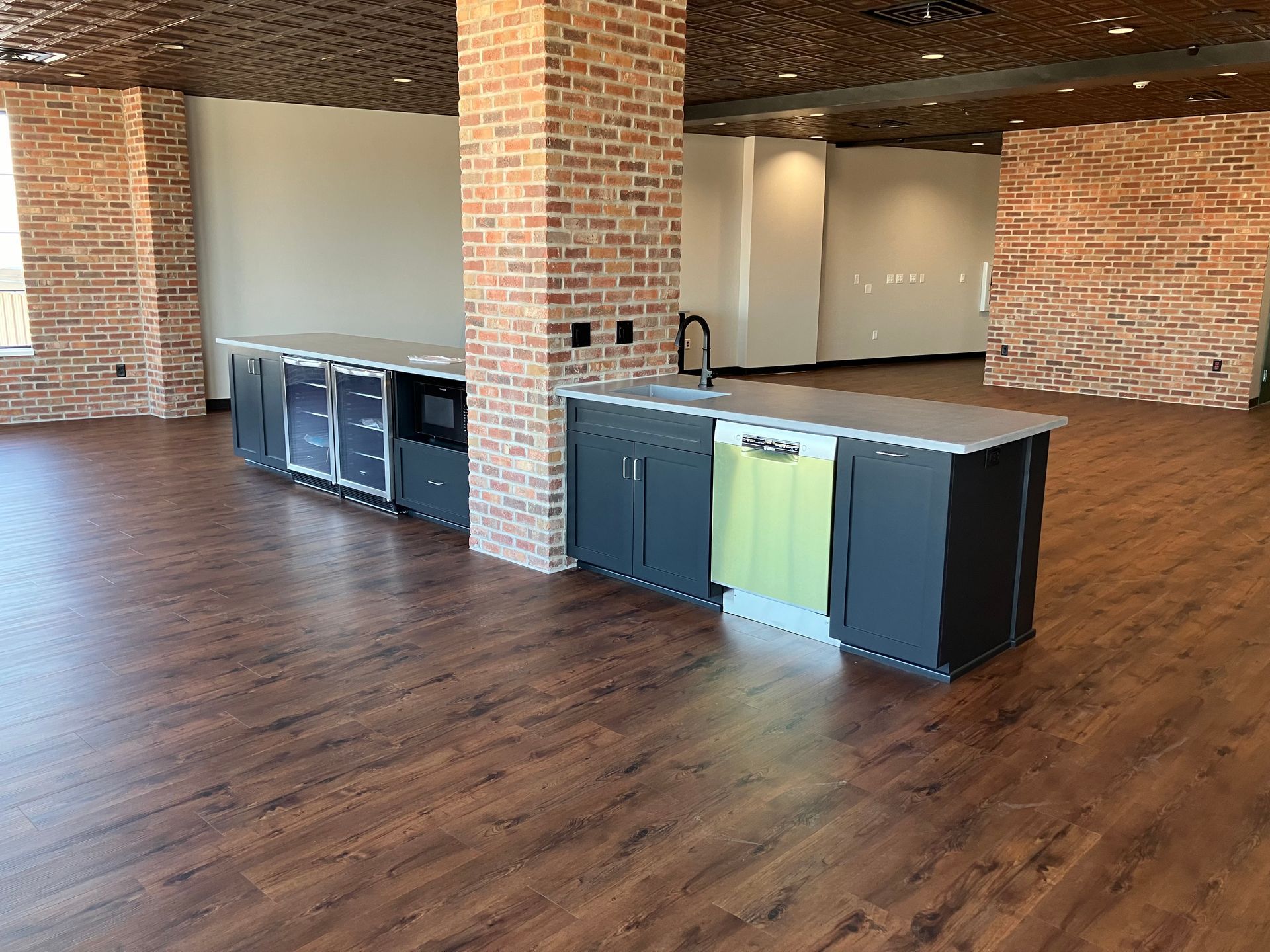 Empty room with a kitchen island; brick columns, wooden floors, and a green dishwasher.
