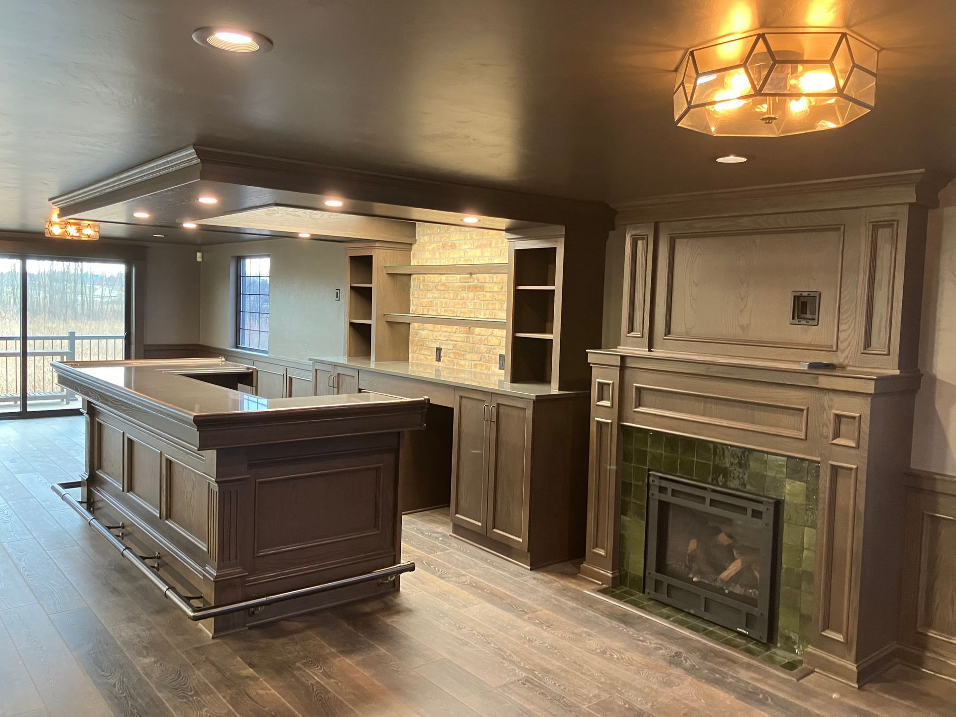 Dark wood finished home bar with fireplace, built-in shelving, and dark-colored ceiling.
