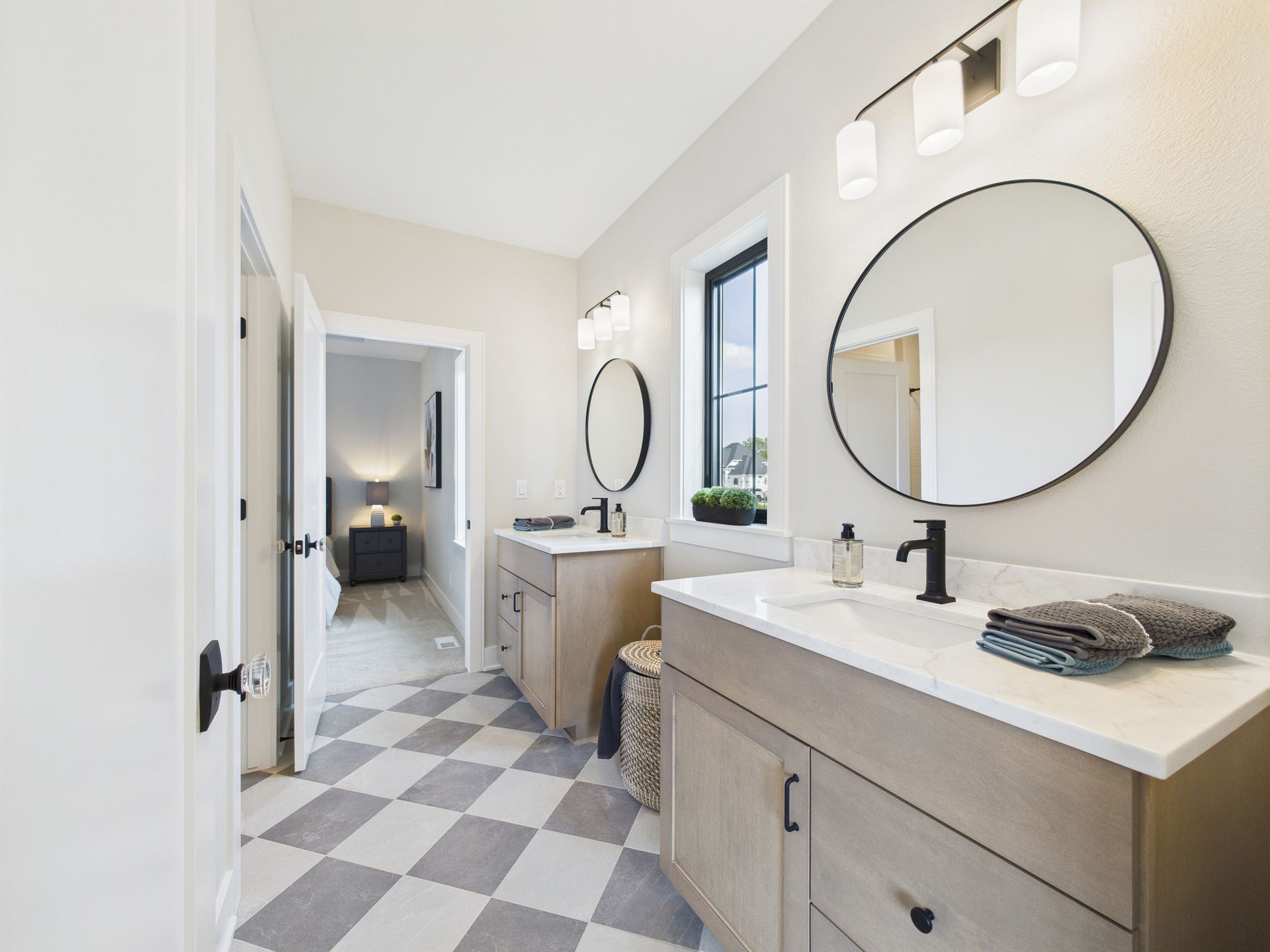 Bathroom with two vanities, round mirrors, black accents, checkered floor.