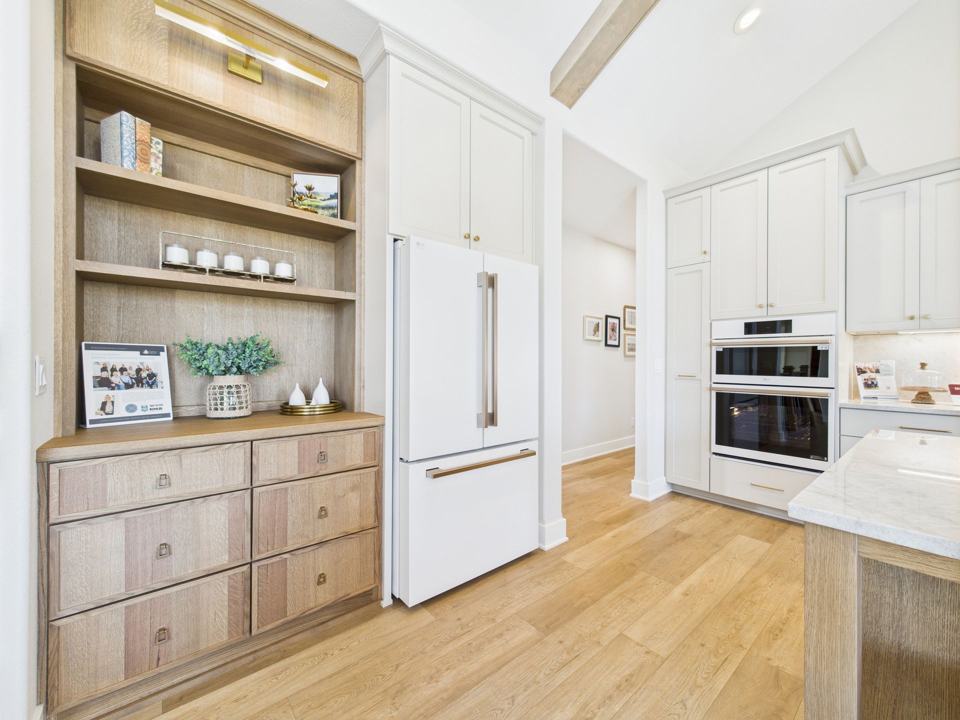 A bright kitchen with wood flooring, white cabinets, and a built-in fridge next to a wooden bookshelf.