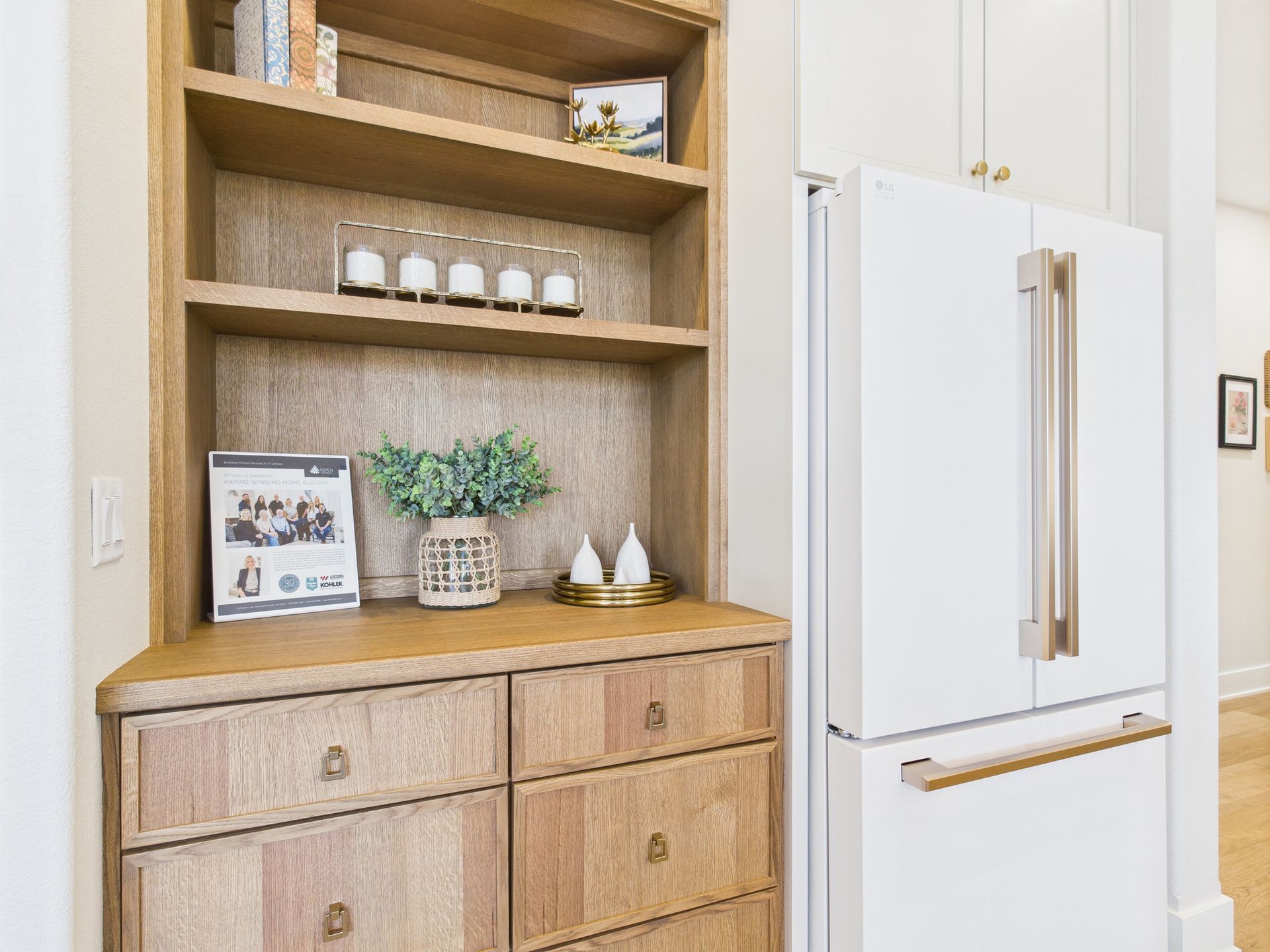 Built-in wooden shelves and cabinets next to a white refrigerator with gold handles in a kitchen.
