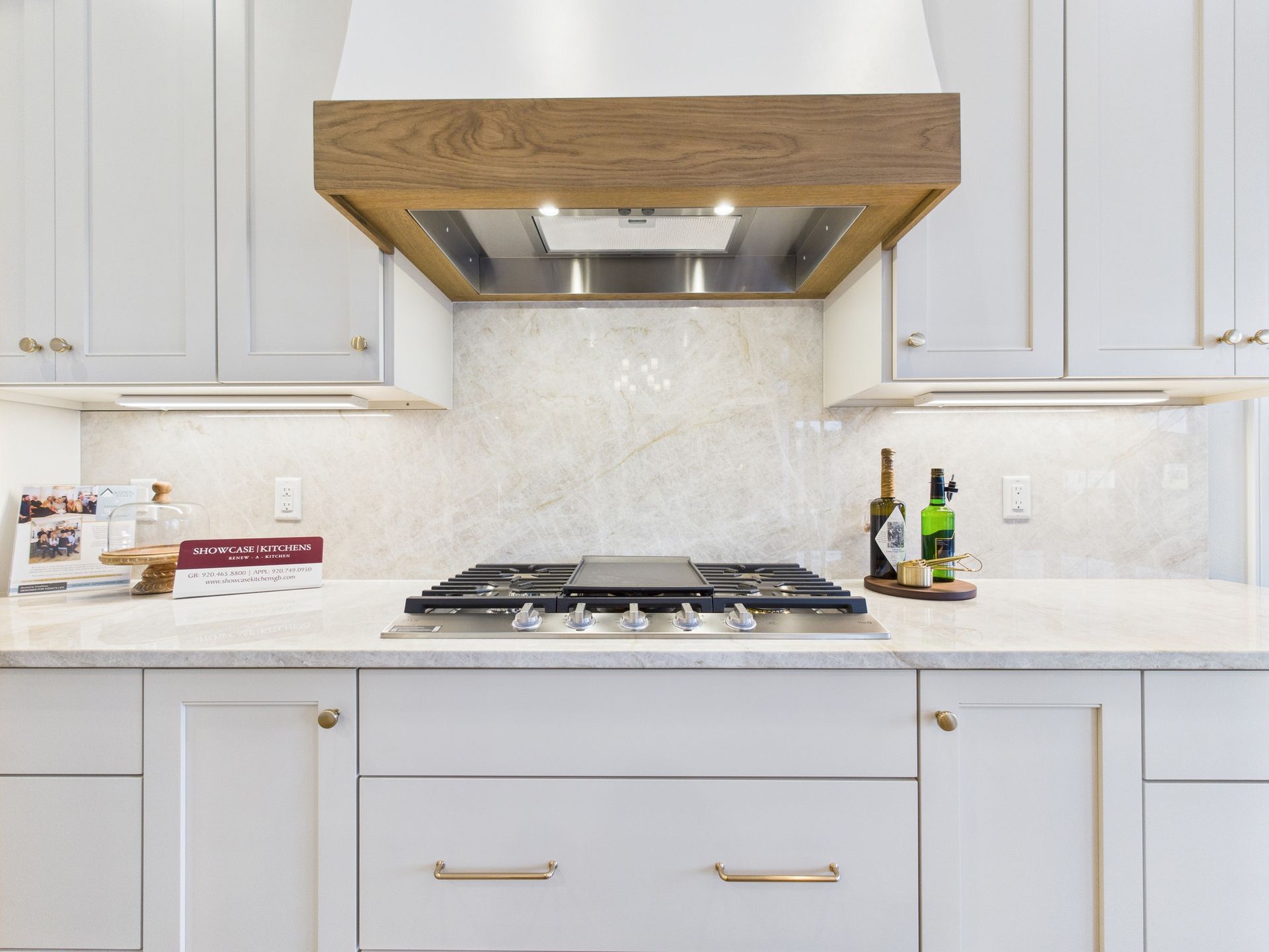 Kitchen with gray cabinets, gas stovetop, wooden range hood, and marble backsplash.