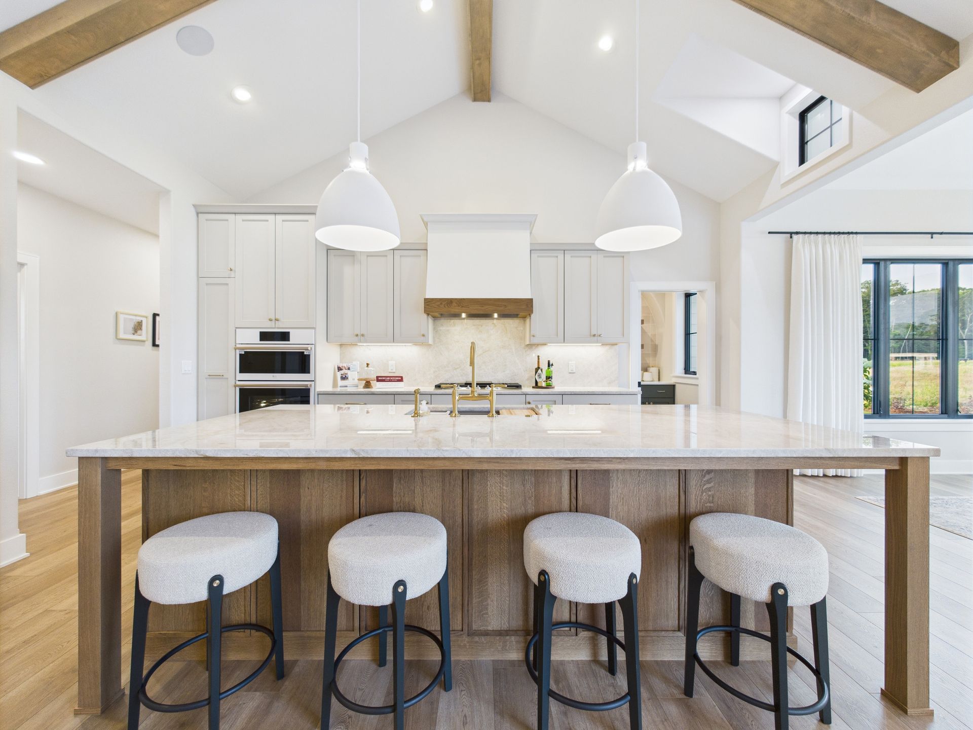 Bright kitchen with a large island, pendant lights, and four upholstered bar stools.