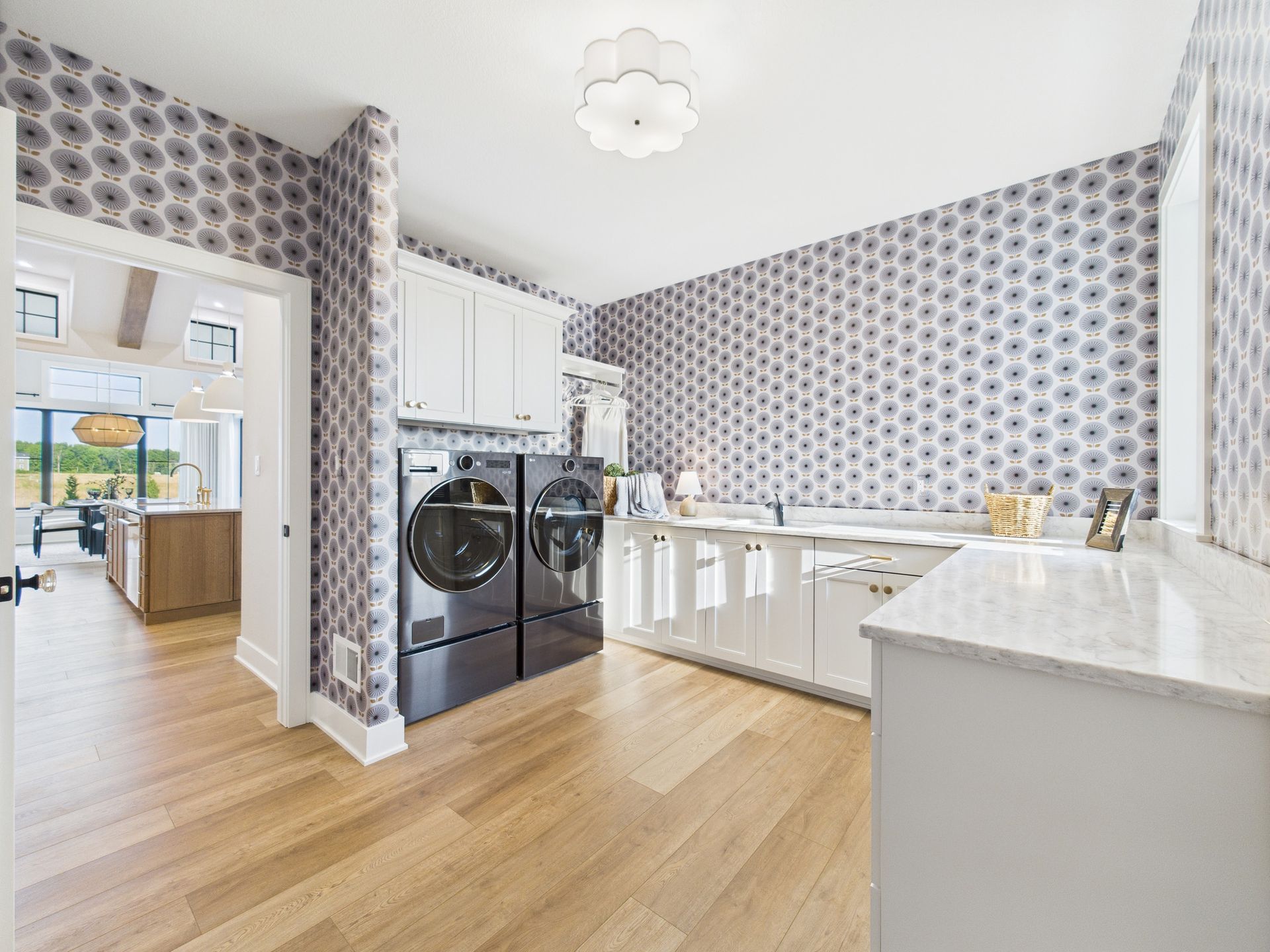 Laundry room with floral wallpaper, white cabinets, and dark appliances. Light wood floors.