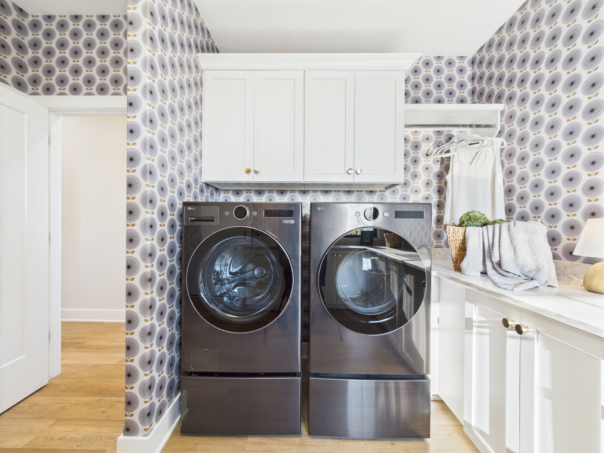 Laundry room with washer and dryer, white cabinets, patterned wallpaper, and a clothes hanging rack.