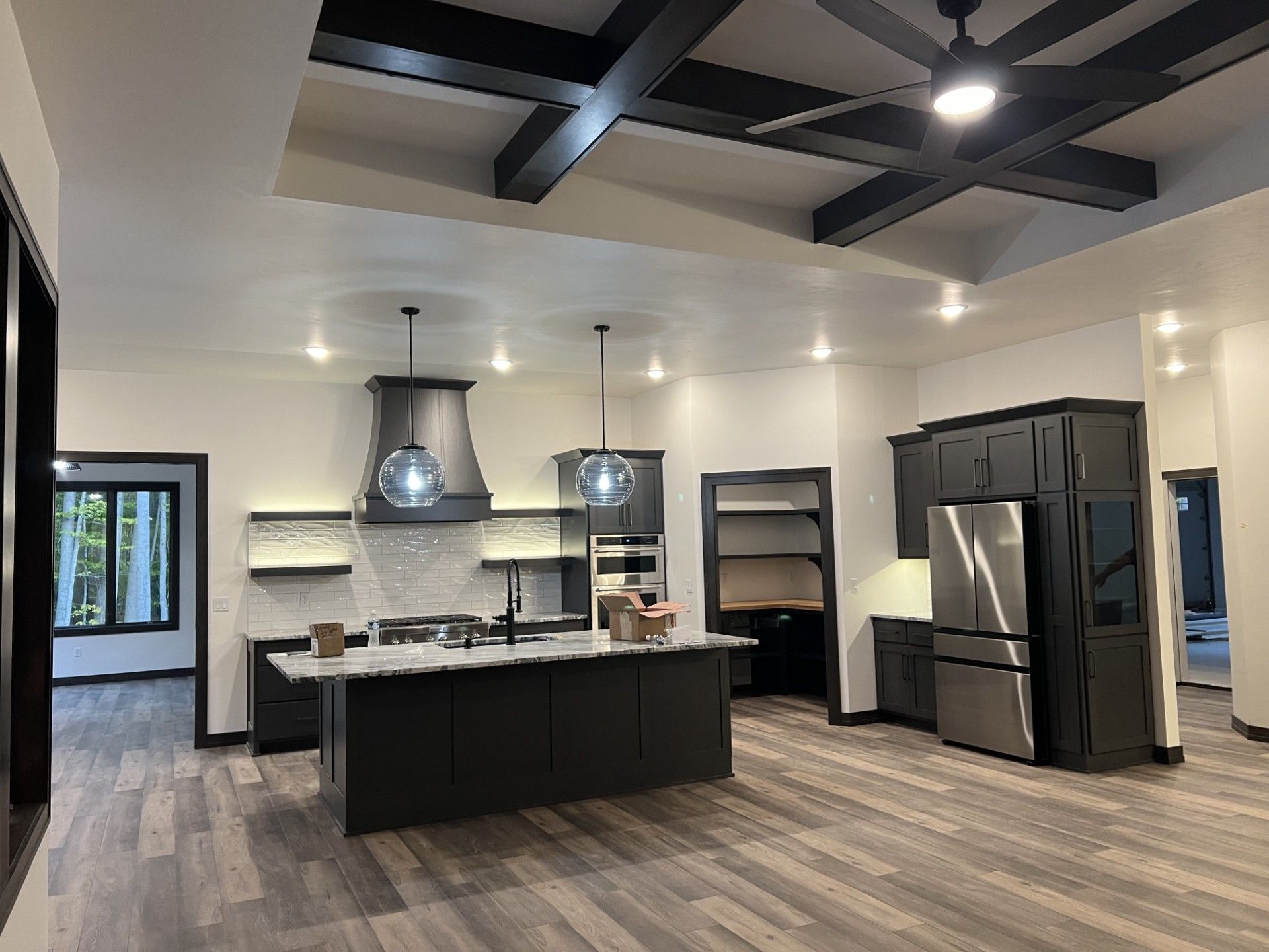 Modern kitchen with black cabinets, island, and ceiling beams. Stainless steel appliances, and hardwood floors.