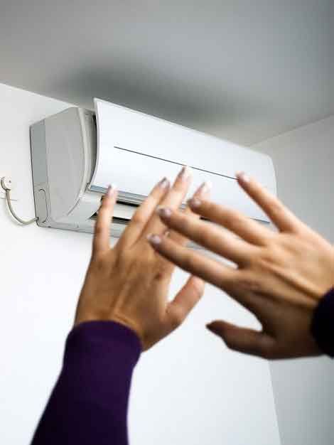 A person is touching a wall mounted air conditioner with their hands.