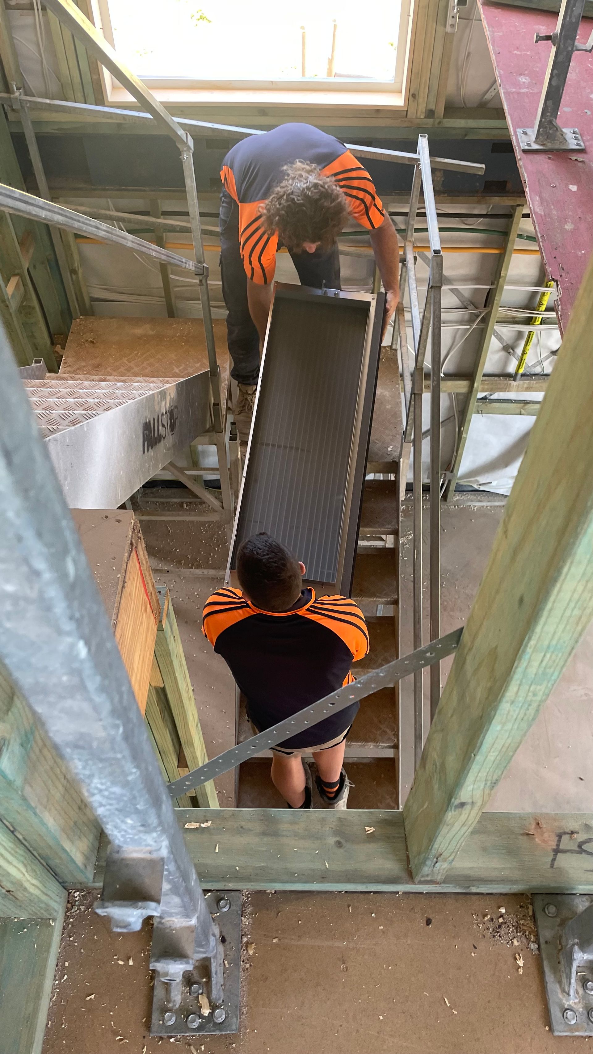 Two men are carrying a conveyor belt up a set of stairs.