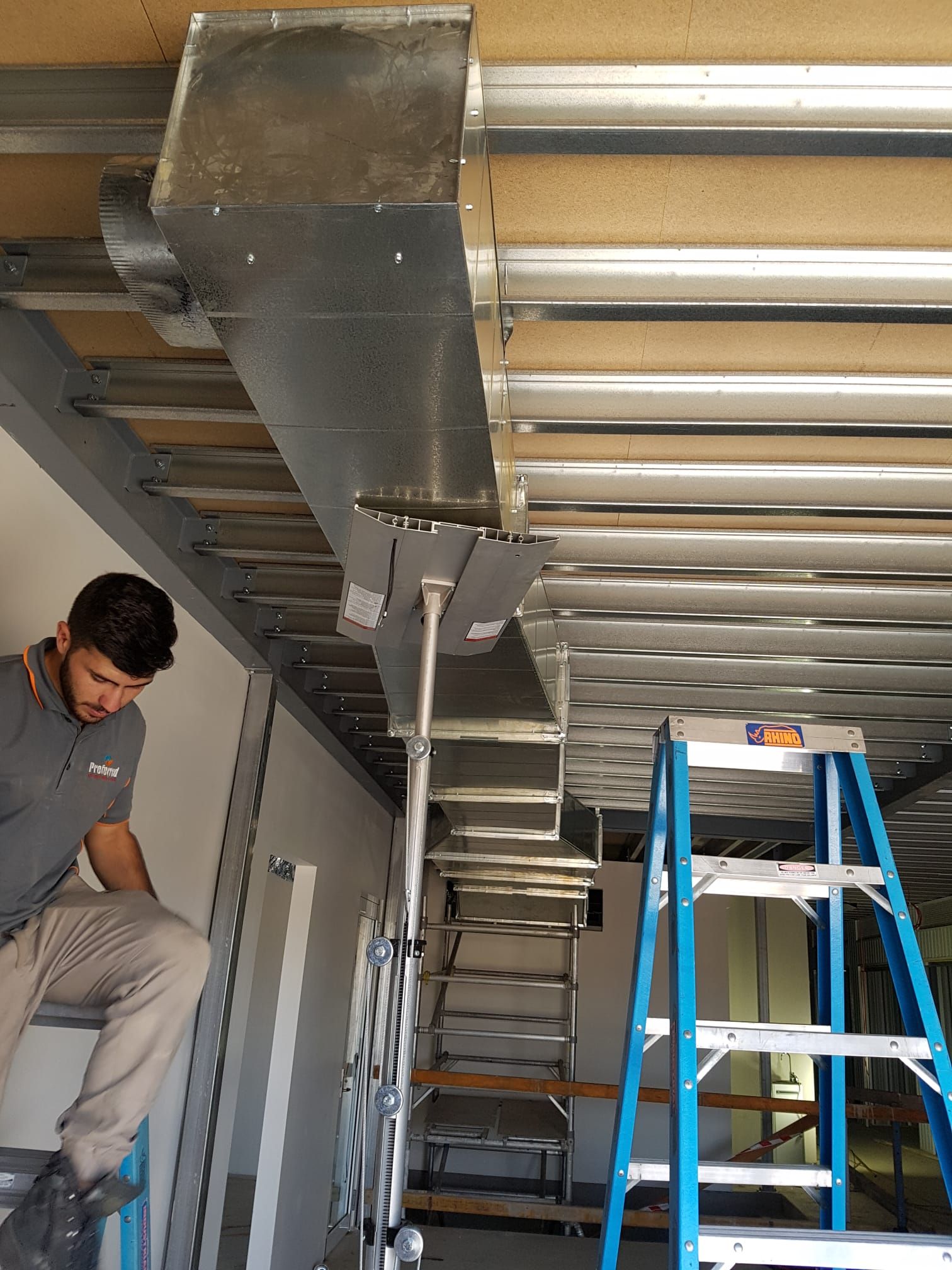 A man is standing on a ladder installing an air conditioner on the side of a building.Blank