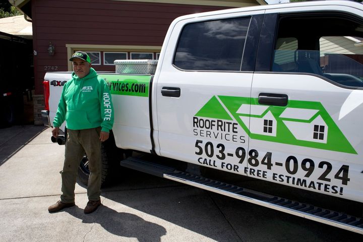 Man in green hoodie stands by a white truck with