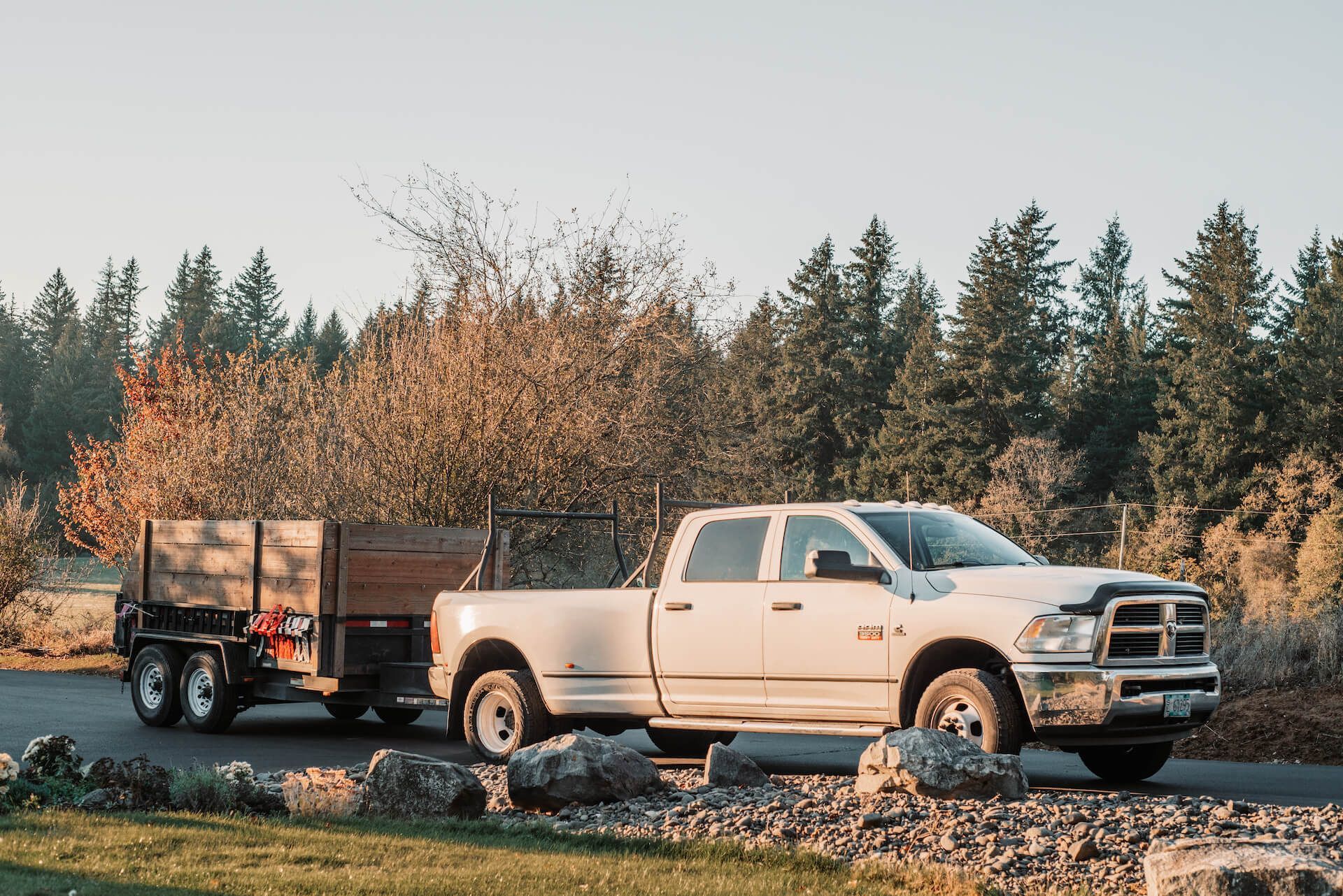 White pickup truck towing a trailer on a road, trees in the background.