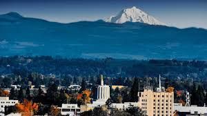 City skyline with snowy mountain peak in the background, blue sky, and fall foliage.