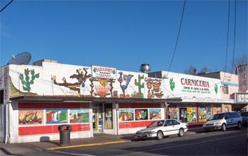 Carniceria restaurant with a mural of cacti and a cowboy, cars parked outside on a sunny day.