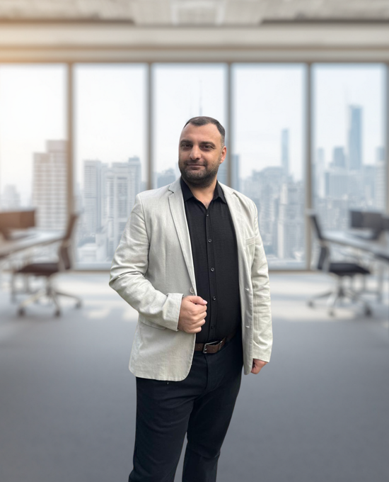 Man in light blazer standing in a modern office with city skyline windows behind him