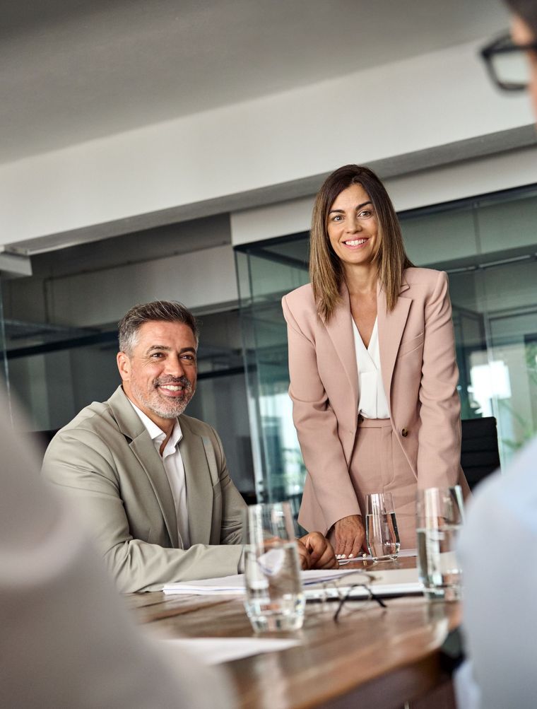Two professionals in a modern conference room, smiling at a meeting table with water glasses and papers.