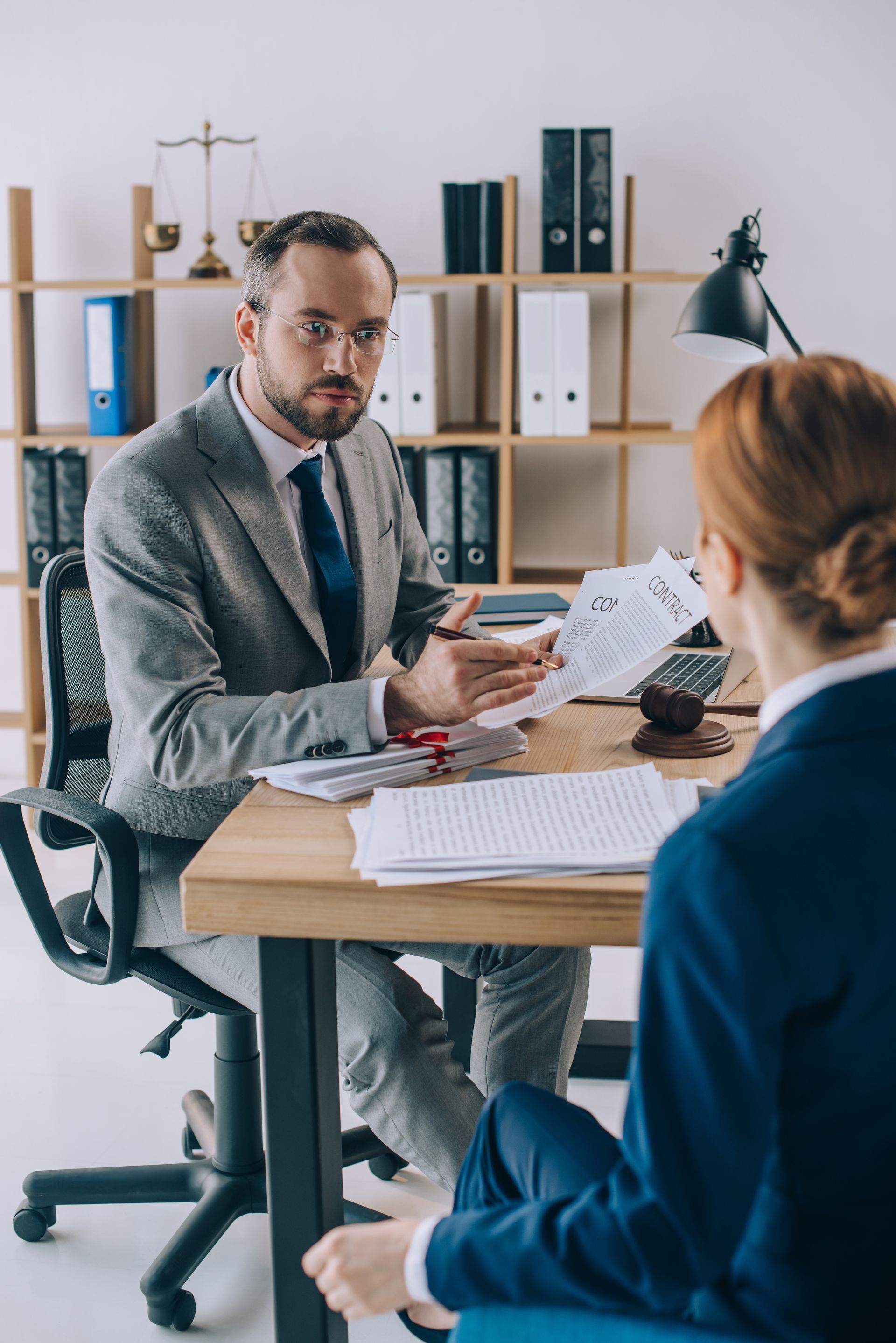 Two people in a meeting across a desk, one holding papers in an office setting