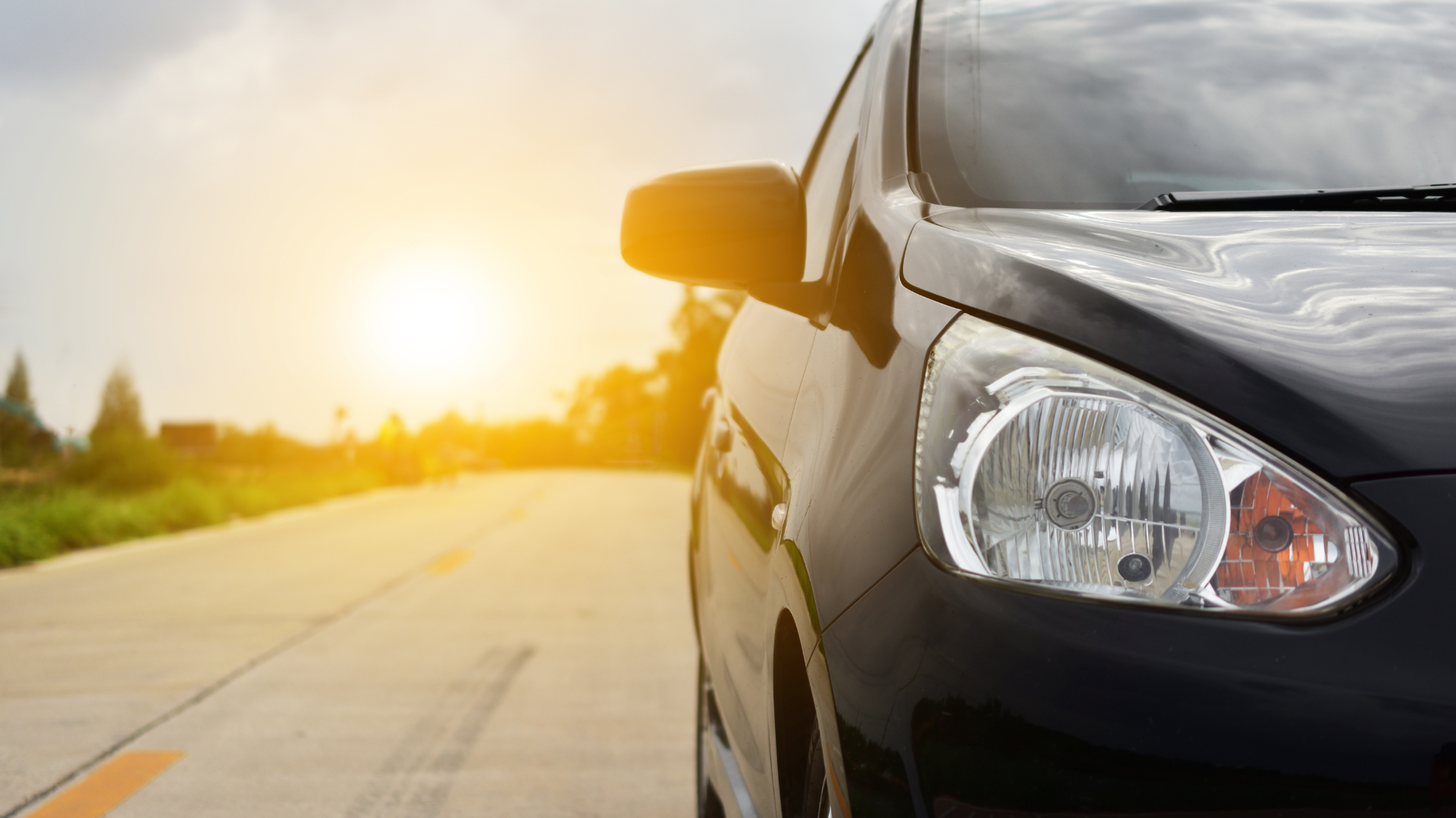 A black car is driving down a road at sunset.