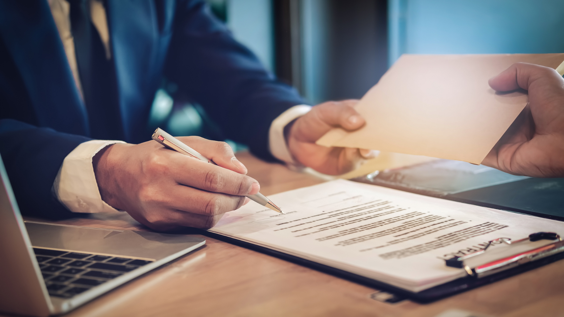 A man in a suit is signing a document while another man looks on.