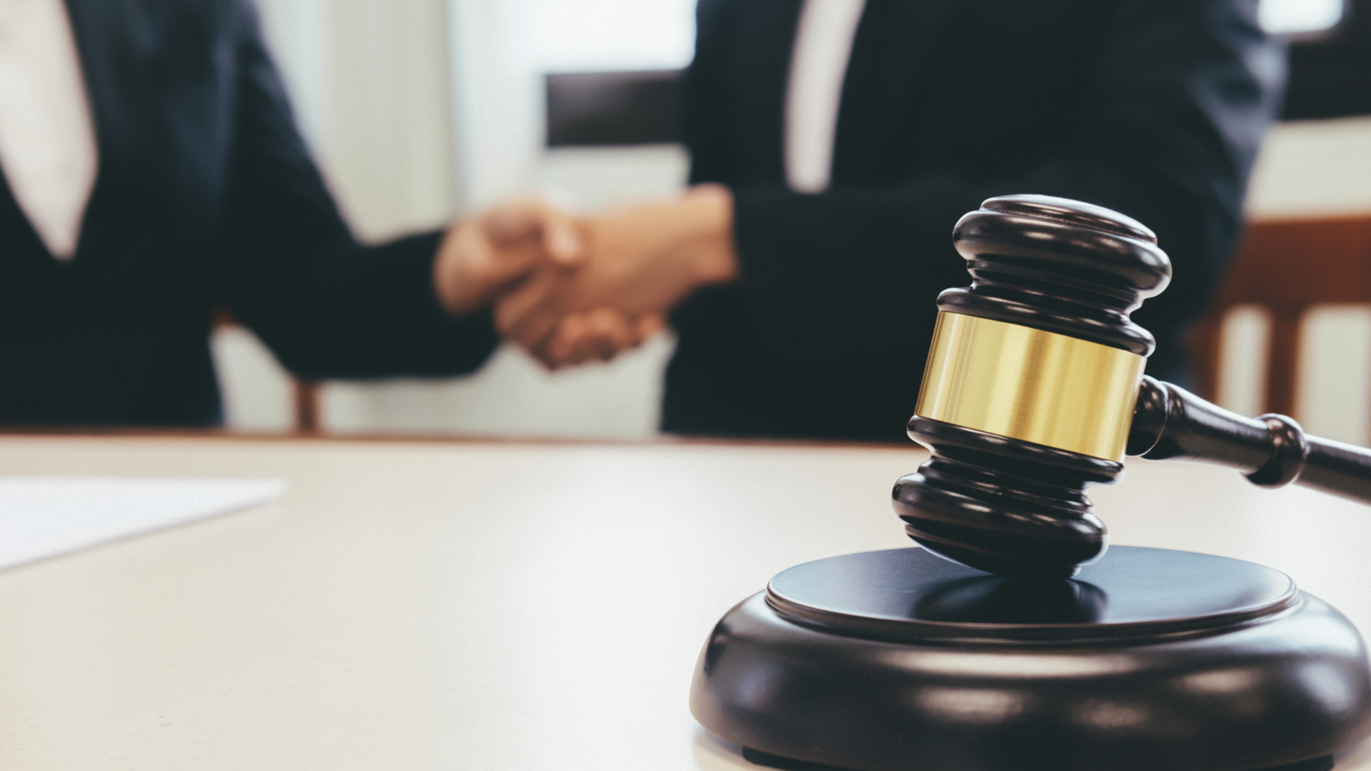 A judge 's gavel is sitting on a table with two people shaking hands in the background.