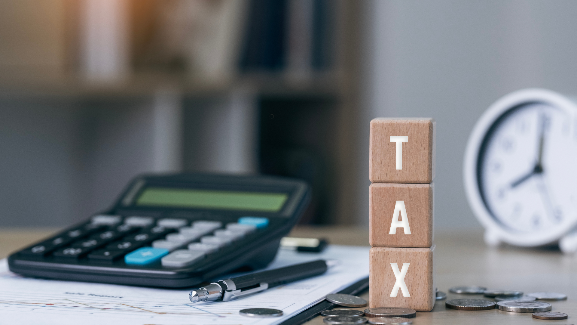 Wooden blocks spelling 'TAX' beside a calculator and coins, symbolizing tax preparation.
