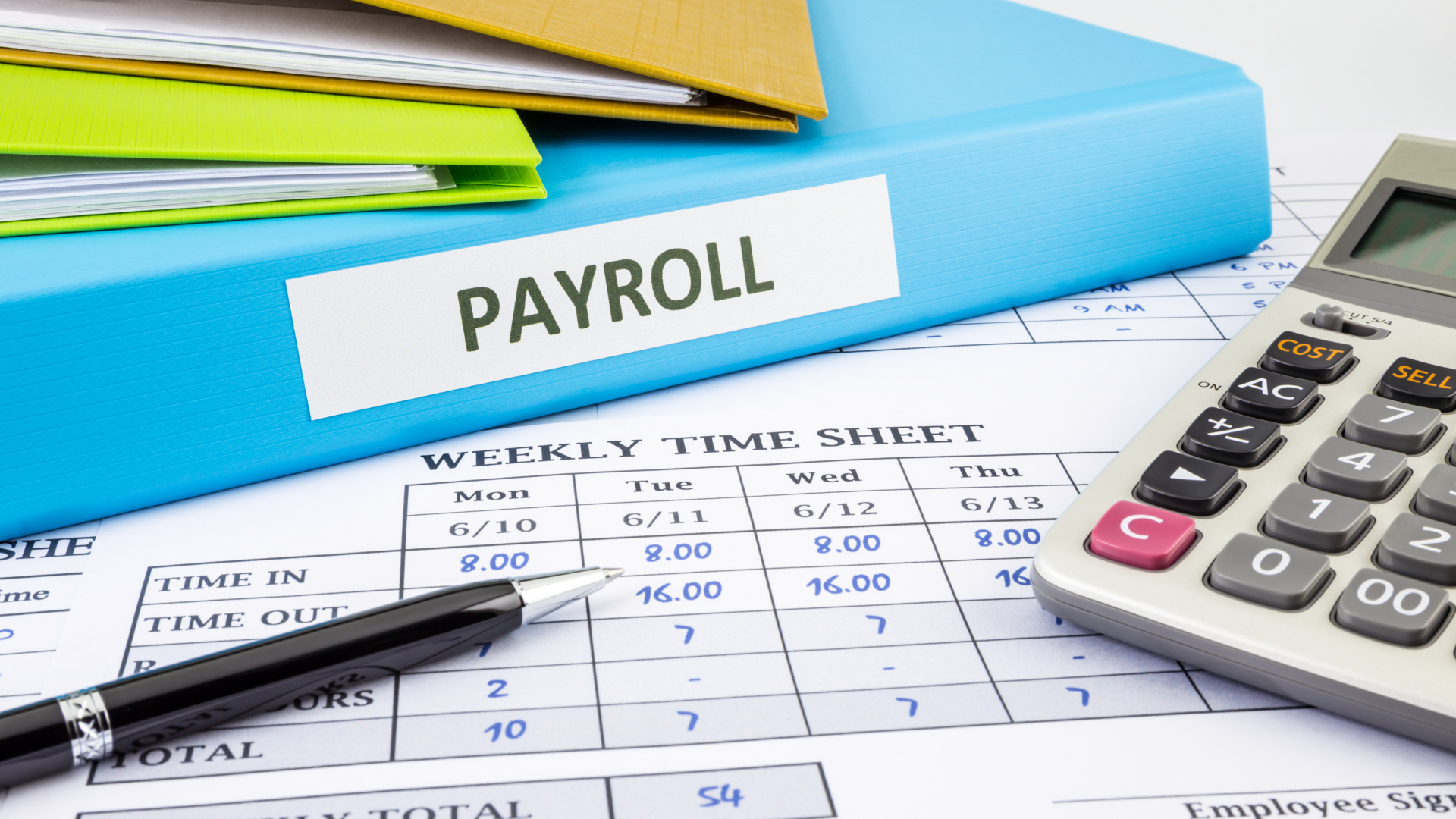 A pen is sitting on top of a payroll binder next to a calculator.