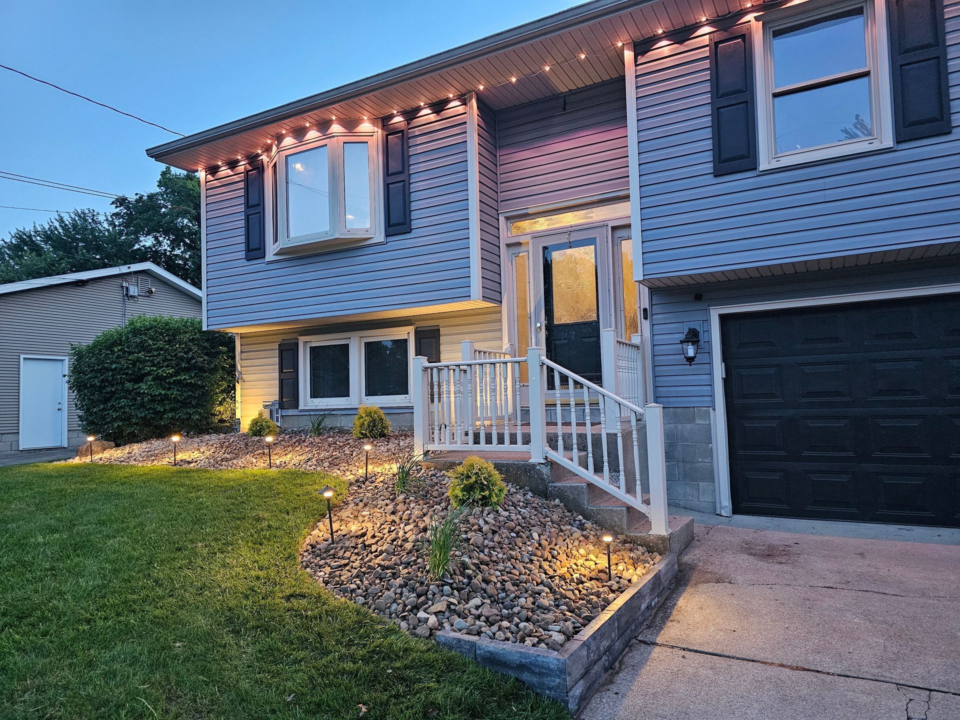 Suburban split-level house at dusk with lit porch, front steps, driveway, and lawn