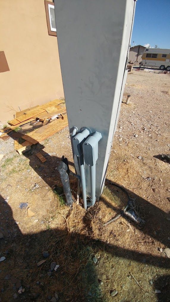 Gray utility box mounted on a concrete pole beside a beige building on a gravel lot