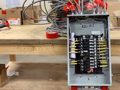 Open electrical control box with labeled wiring on a workbench in a workshop