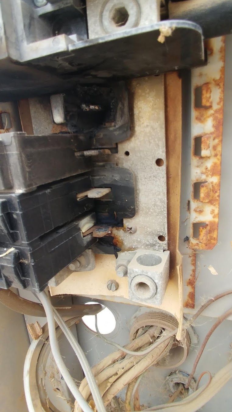 Close-up of a damaged electrical breaker panel with burnt components and exposed wires