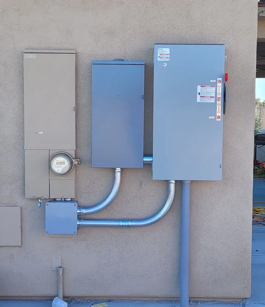 Blue utility boxes and electrical meter mounted on a beige exterior wall with conduit pipes.