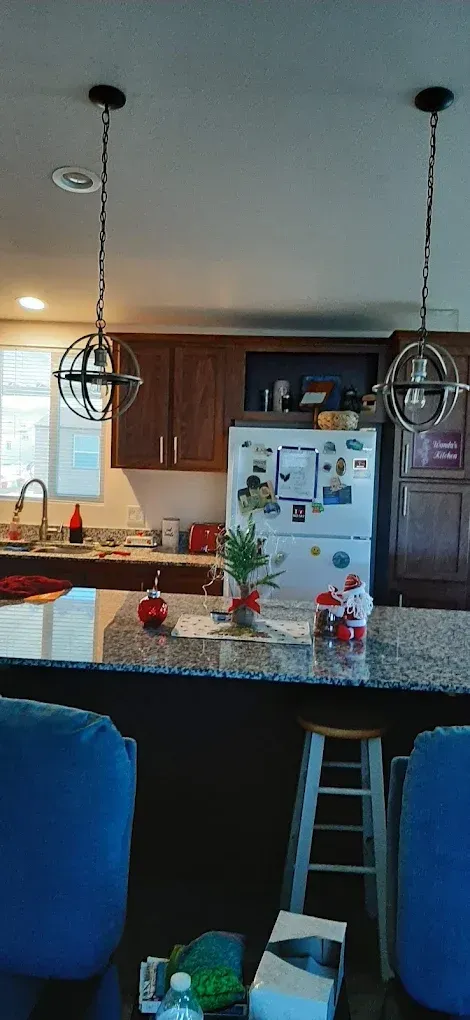 Kitchen with granite island, white fridge, dark wood cabinets, pendant lights, and blue barstools