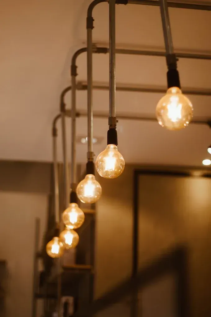 Row of glowing Edison bulbs hanging from dark pipes in a warm indoor setting