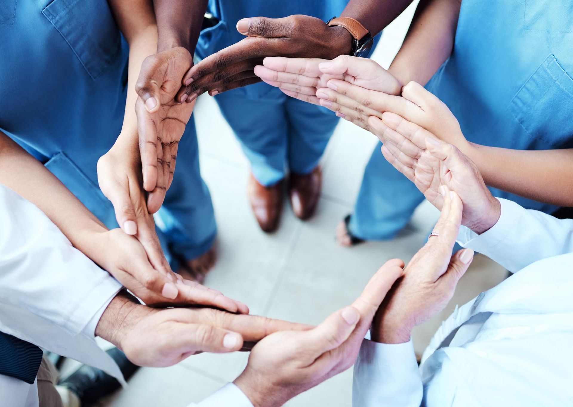 Healthcare workers linking hands in a circle, viewed from above in blue uniforms