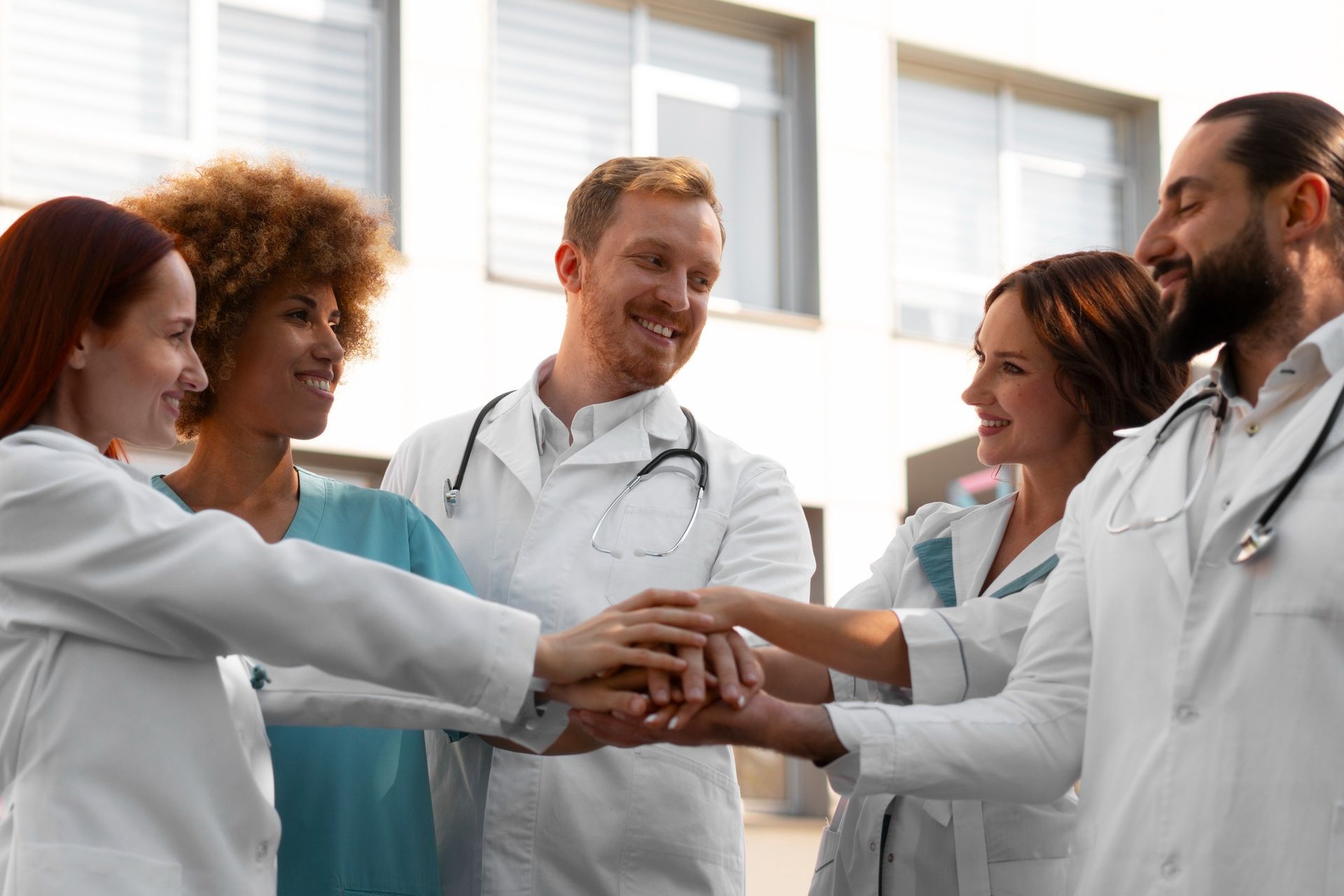 Medical team in white coats stacking hands in a bright hospital room