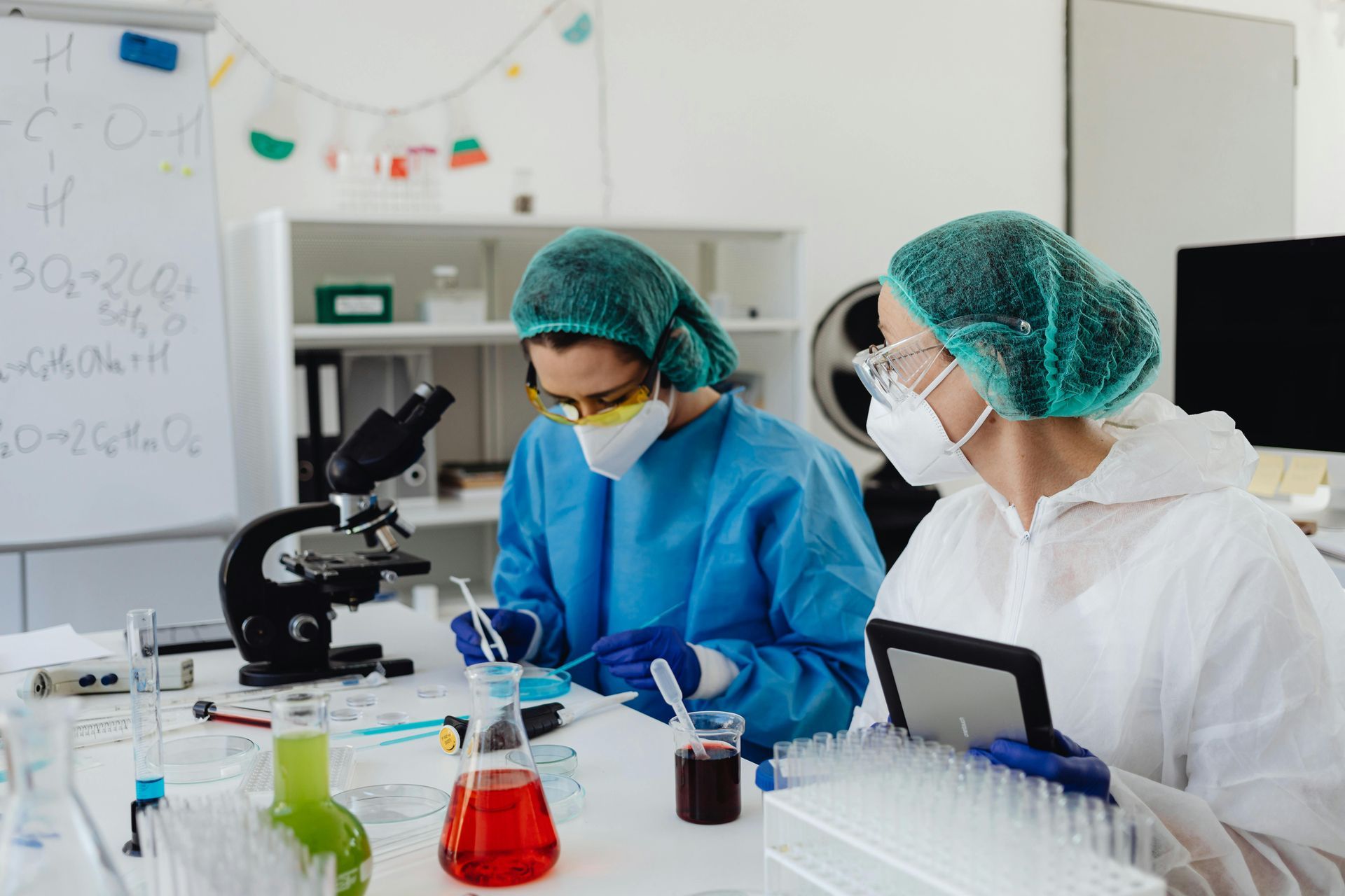 Two lab technicians in protective gear working at a microscope in a bright laboratory